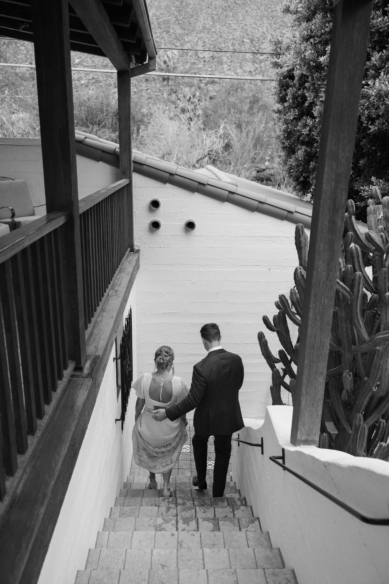 Black and white photo of a couple in formal attire holding hands while descending outdoor stone steps.