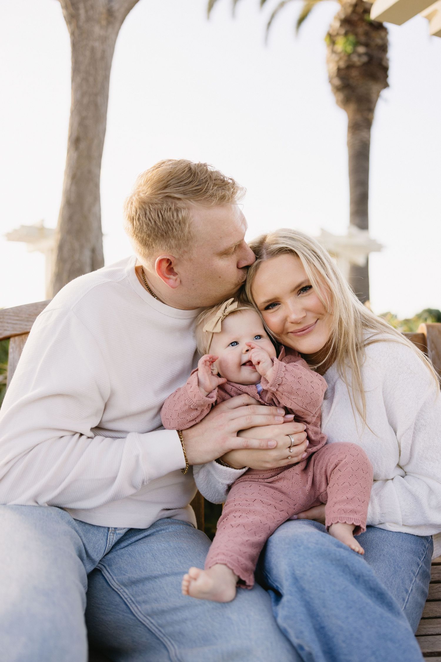 Family snuggling together on a bench surrounded by palm trees during a sunny afternoon.