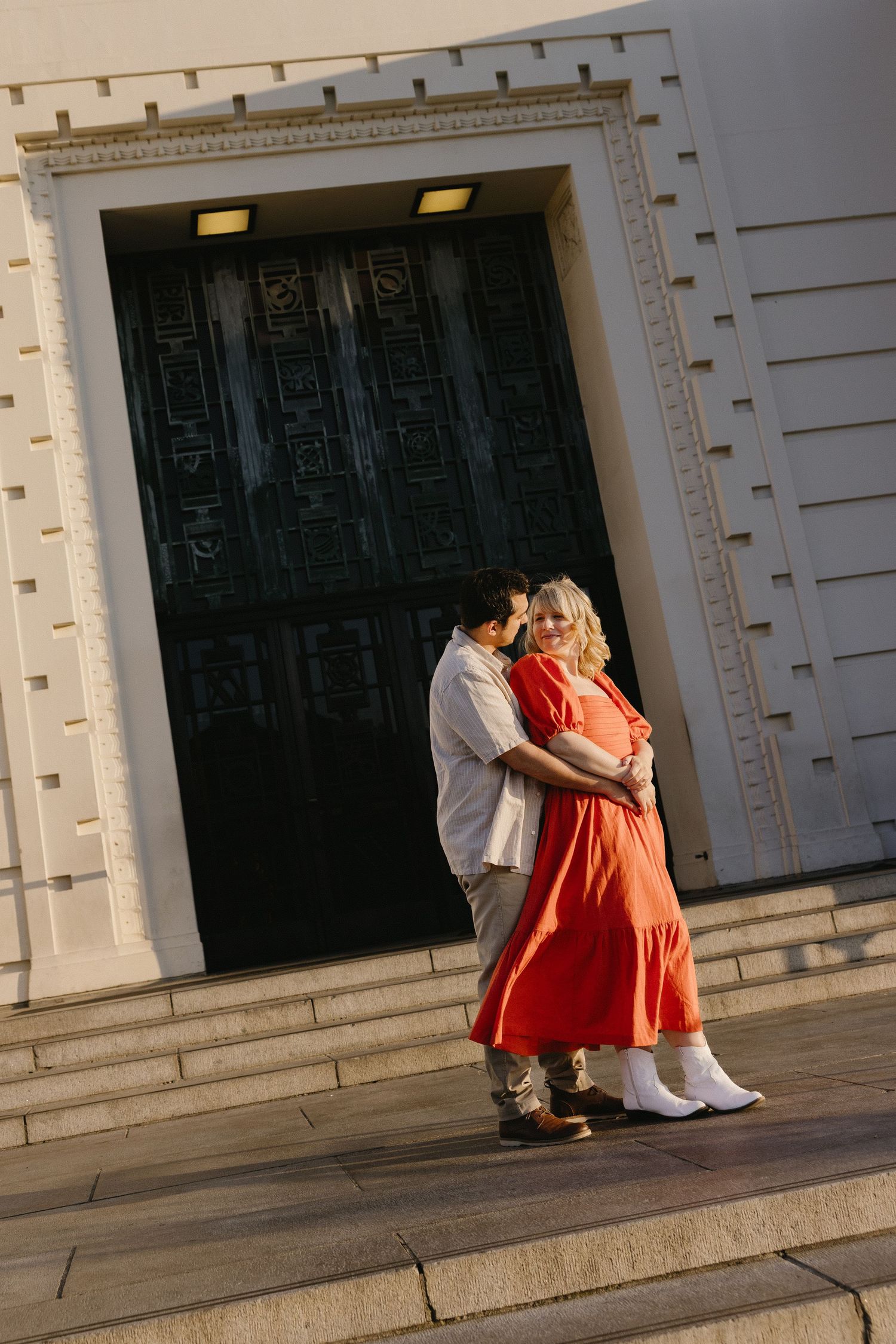 Romantic couple embracing in front of an ornate building entrance with dramatic lighting.