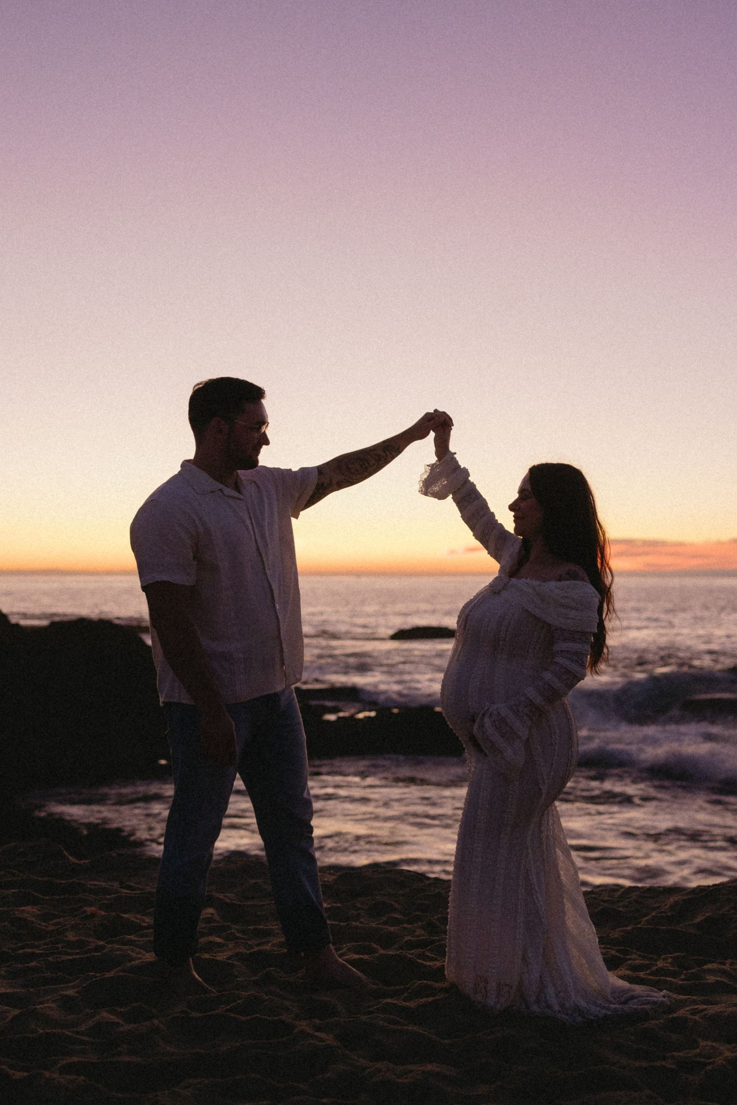 Silhouetted couple dancing on beach at sunset with ocean waves in background.