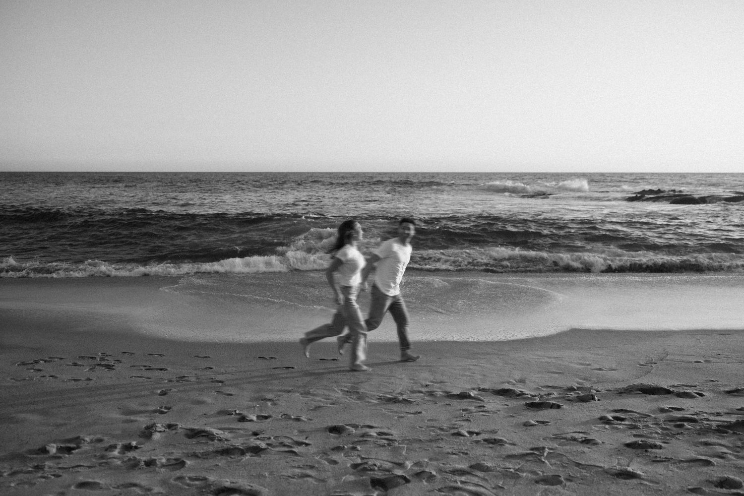 People strolling on a scenic beach with rocky outcrops and ocean waves at dusk.
