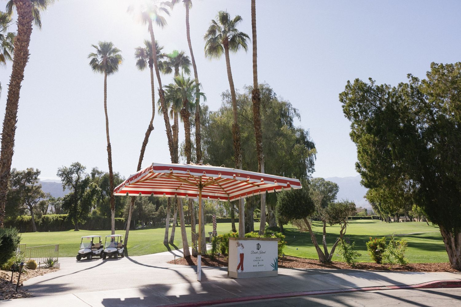 Golf cart shelter with red striped canopy surrounded by tall palm trees on a sunny golf course.