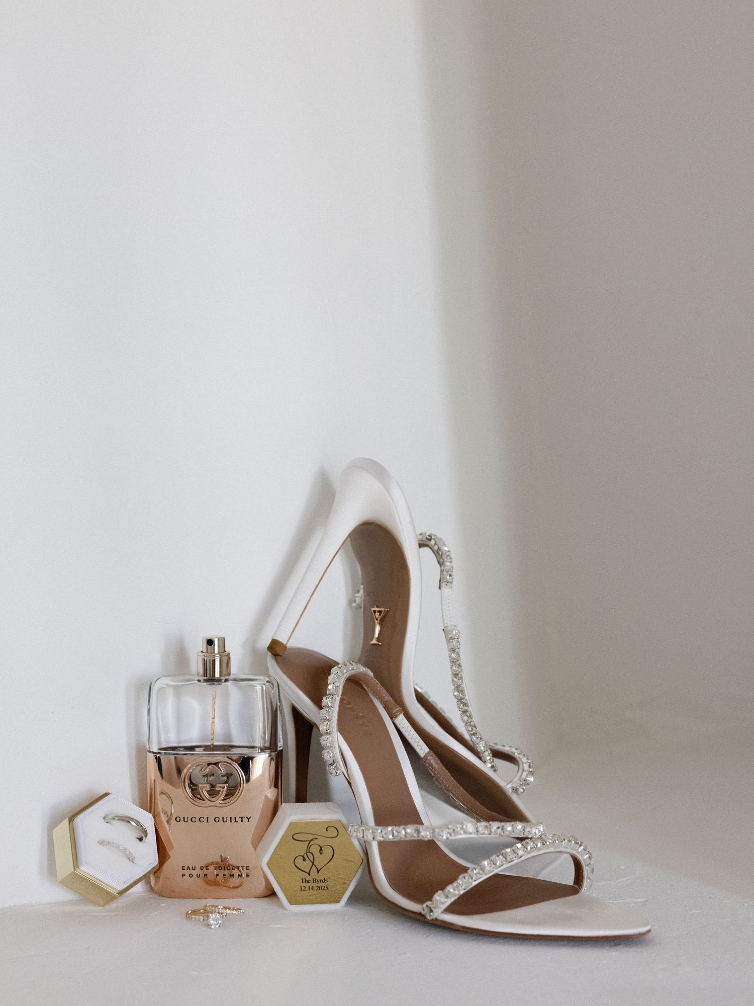 Wedding accessories including white heels, perfume bottles and jewelry arranged on a light surface.