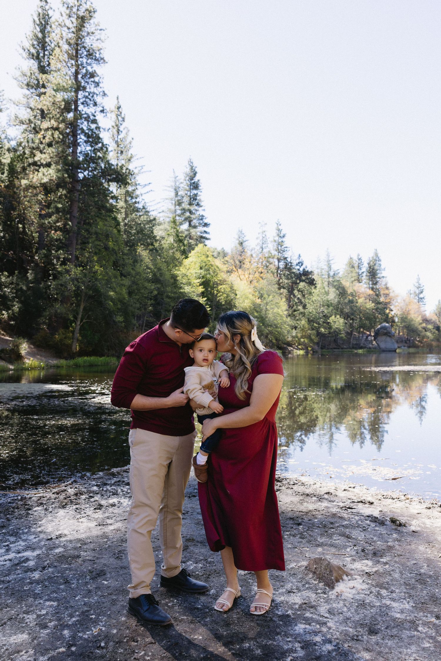 Intimate family moment captured by a serene lake surrounded by evergreen trees.