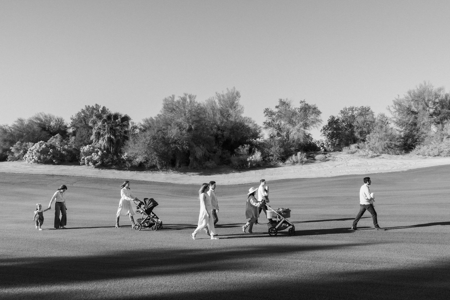 Black and white panoramic shot of people walking across a rolling green field.