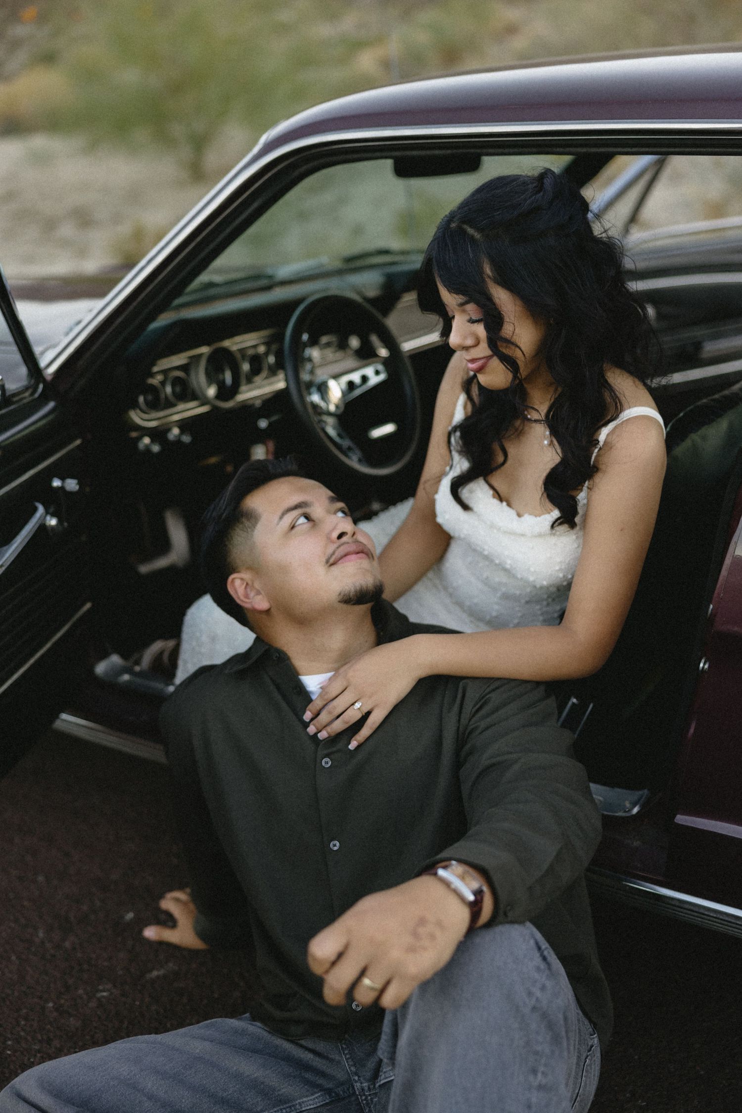 Couple sharing playful moments inside vintage car against desert backdrop.
