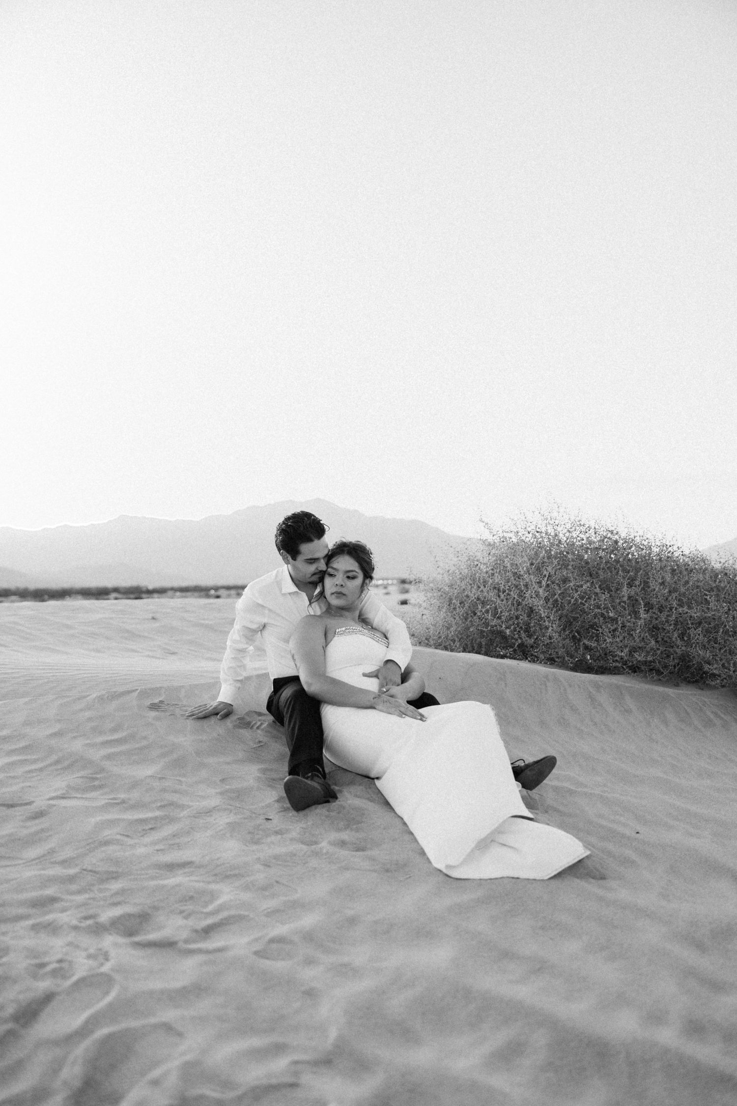 Black and white photo of couple sitting together on desert sand dunes.
