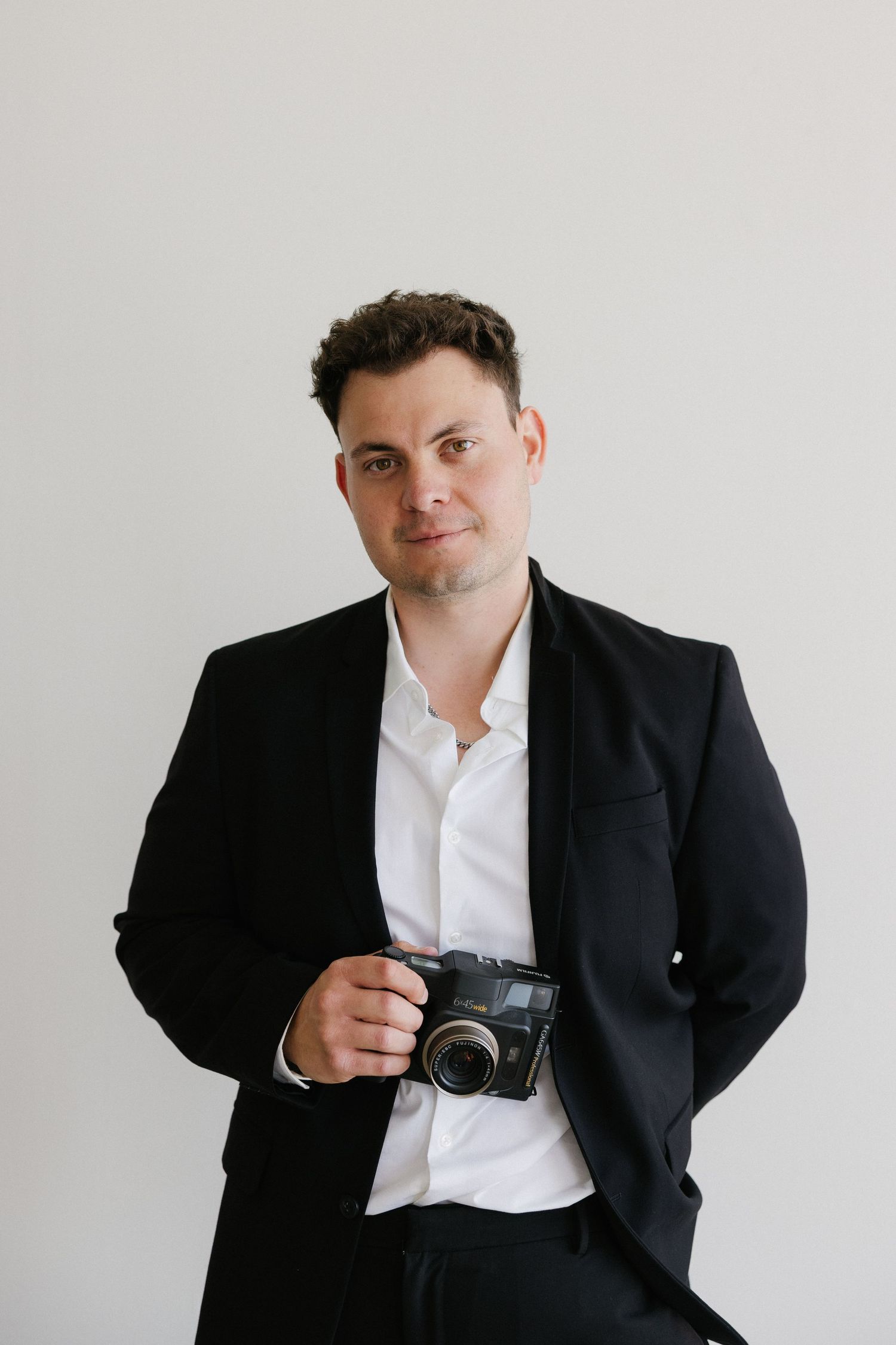 A professional man in a black blazer and white shirt holds a vintage film camera against a clean white background.