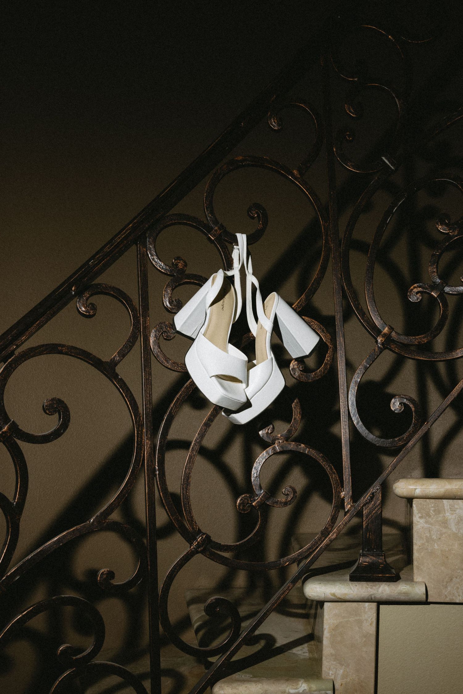 White bridal shoes displayed on ornate wrought iron railings in dramatic lighting.