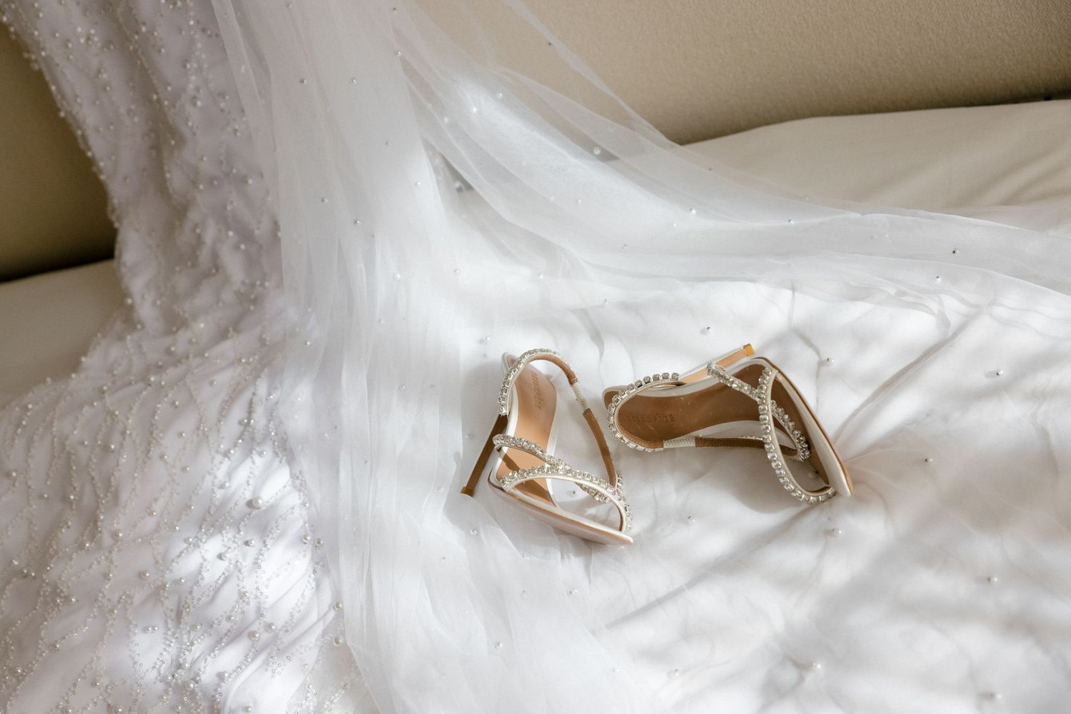 Bridal heels rest delicately on white lace wedding dress fabric.