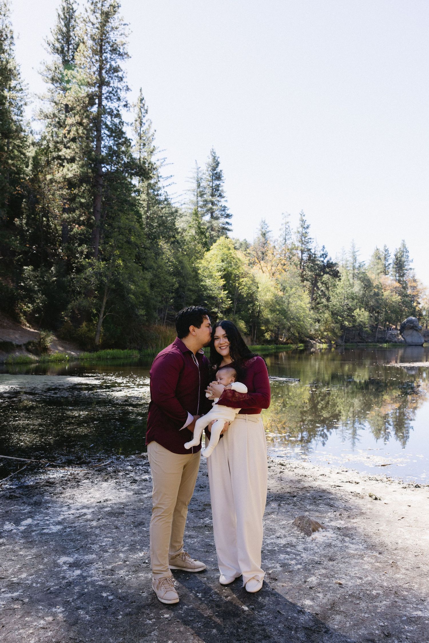 Sweet family moment captured during outdoor photoshoot by peaceful lake.