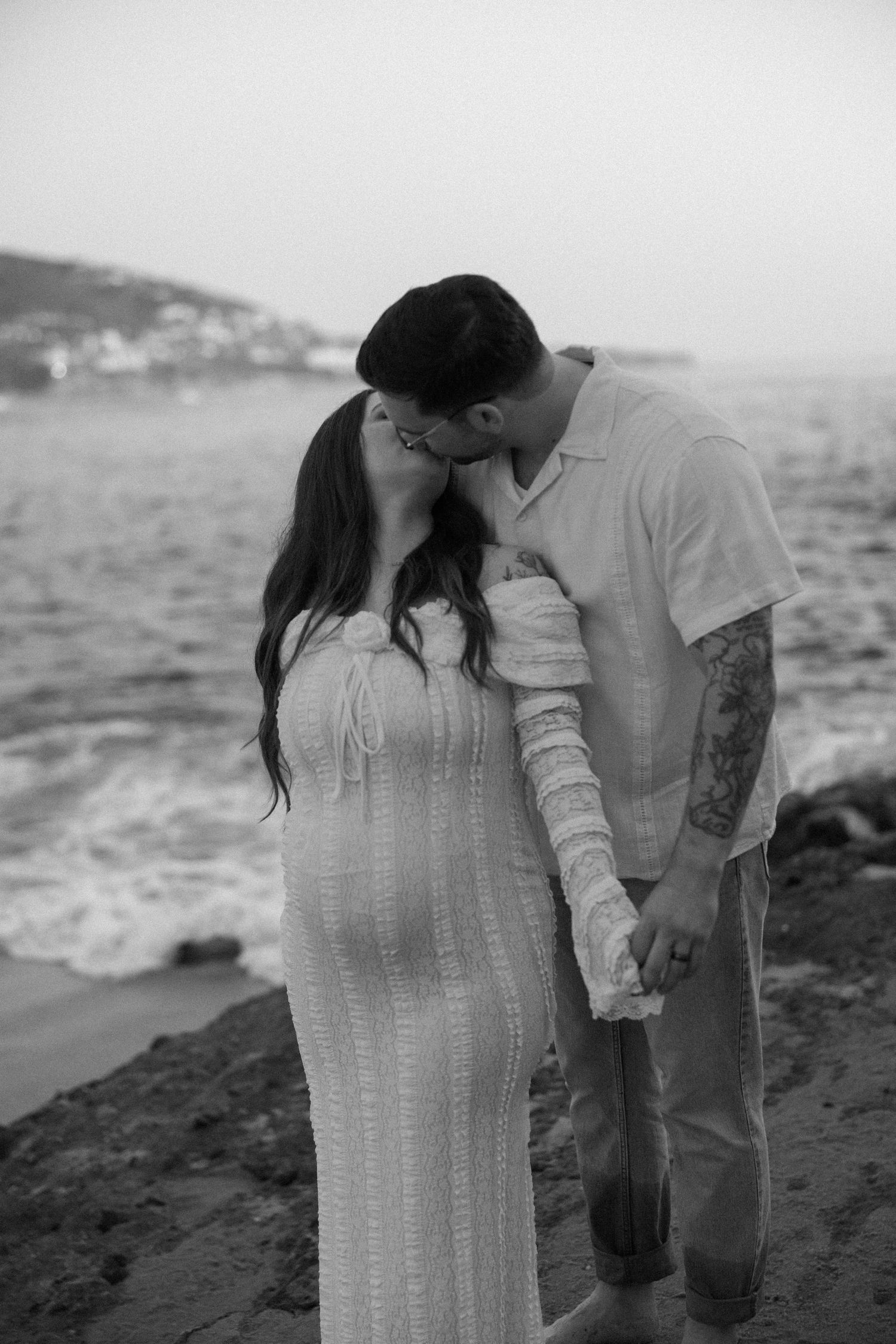 Romantic couple in white sharing intimate moment by ocean cliffs.