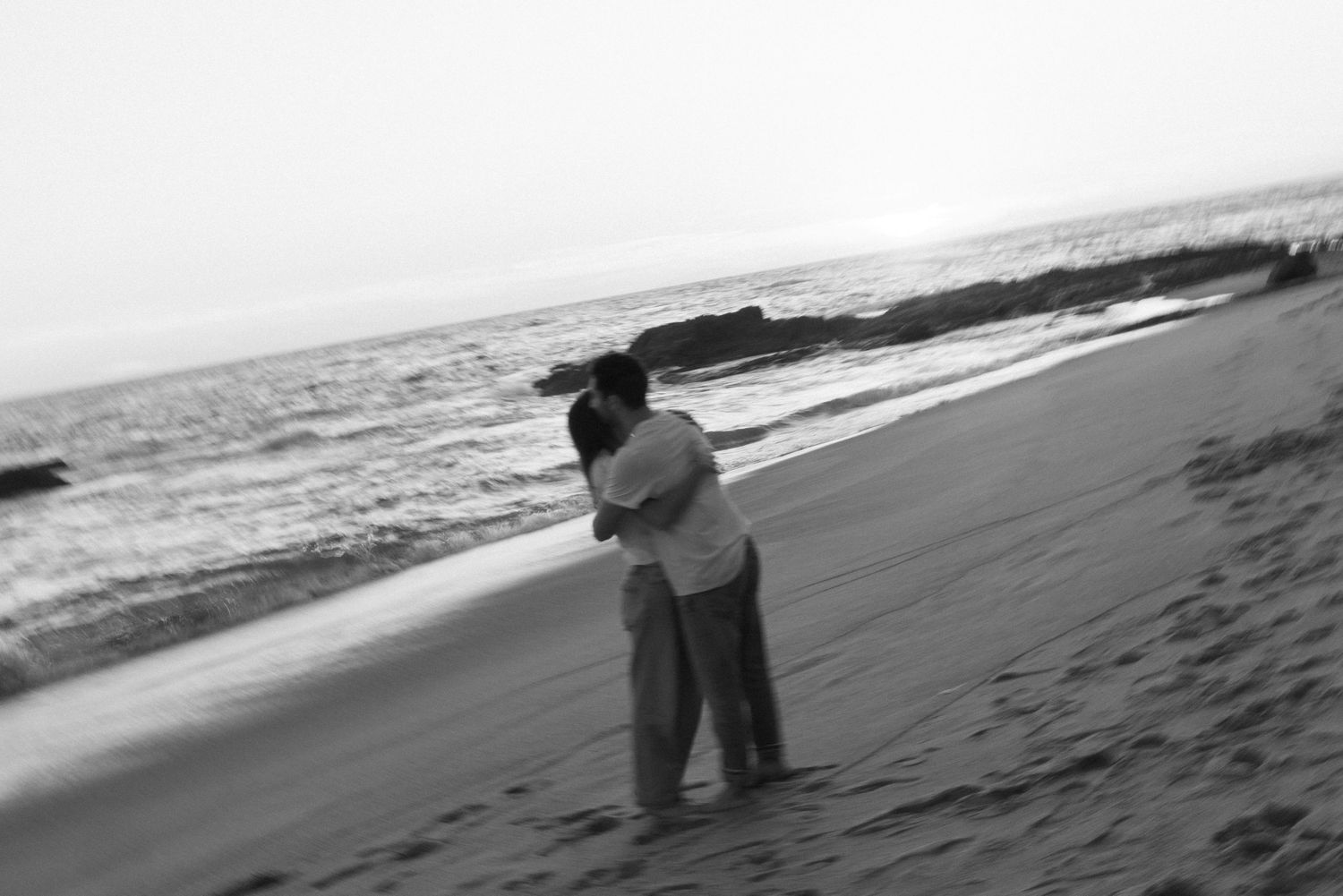 Black and white photo of people exploring a rugged coastal beach landscape.