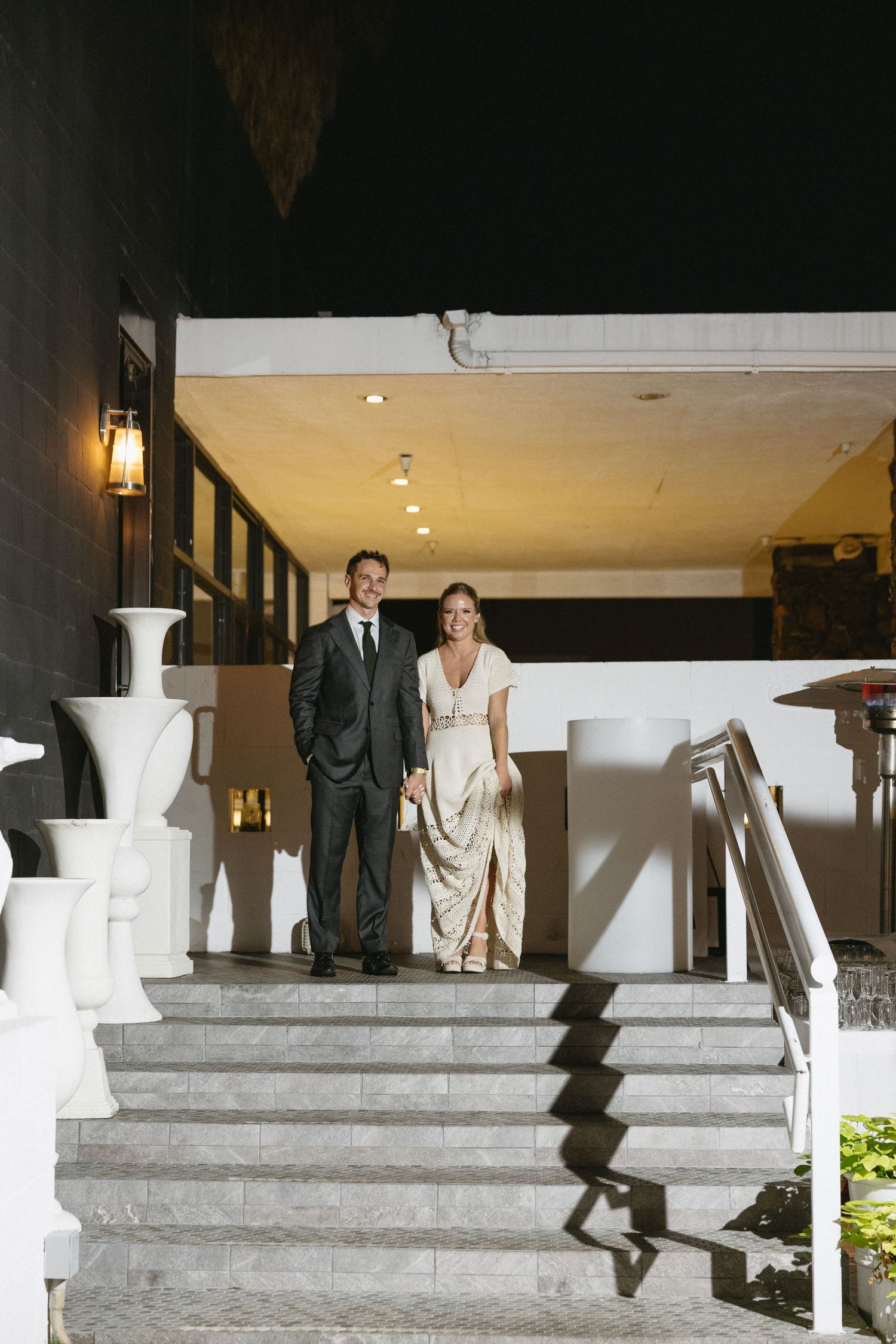Elegant couple in formal attire descending marble stairs at a sophisticated venue during evening event.