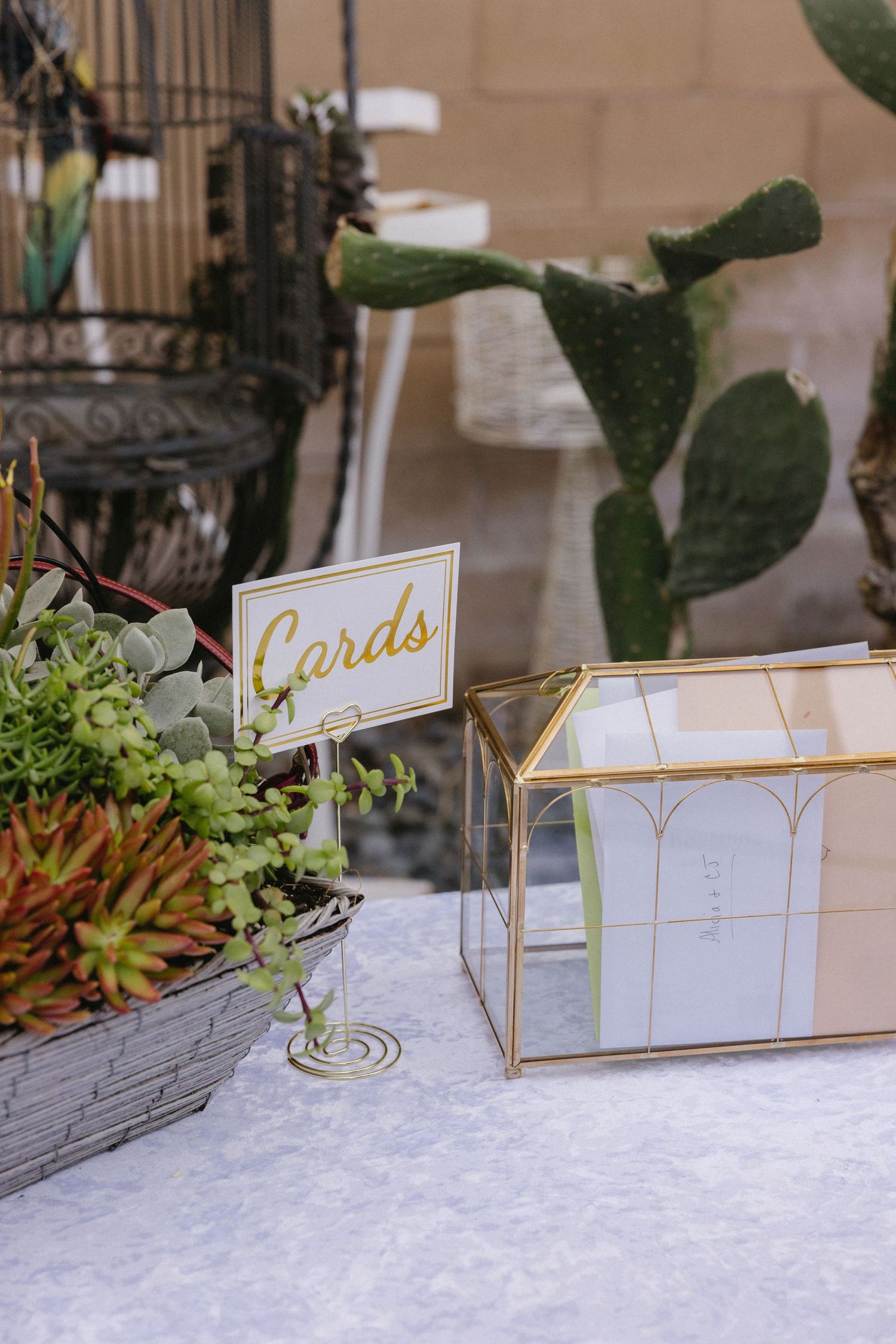 Wedding card box display with gold geometric terrarium, succulent centerpiece, and decorative Cards sign on white table.
