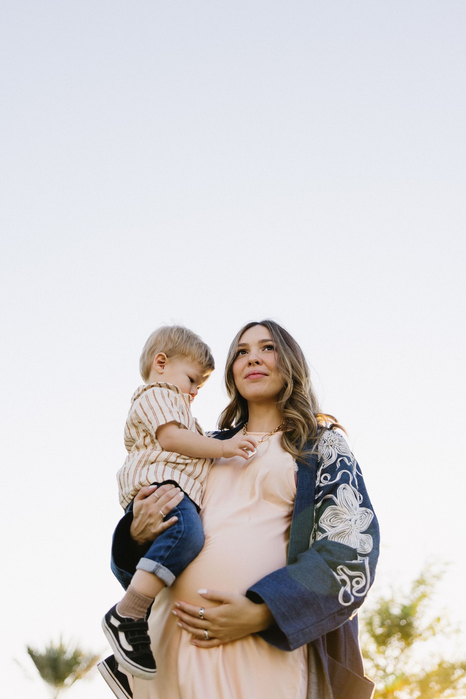 Family moment captured against bright sky with denim jacket and pink dress.