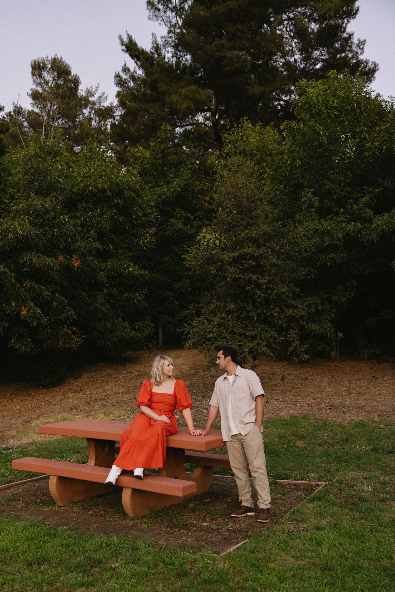 Couple sitting on red benches surrounded by trees at sunset.