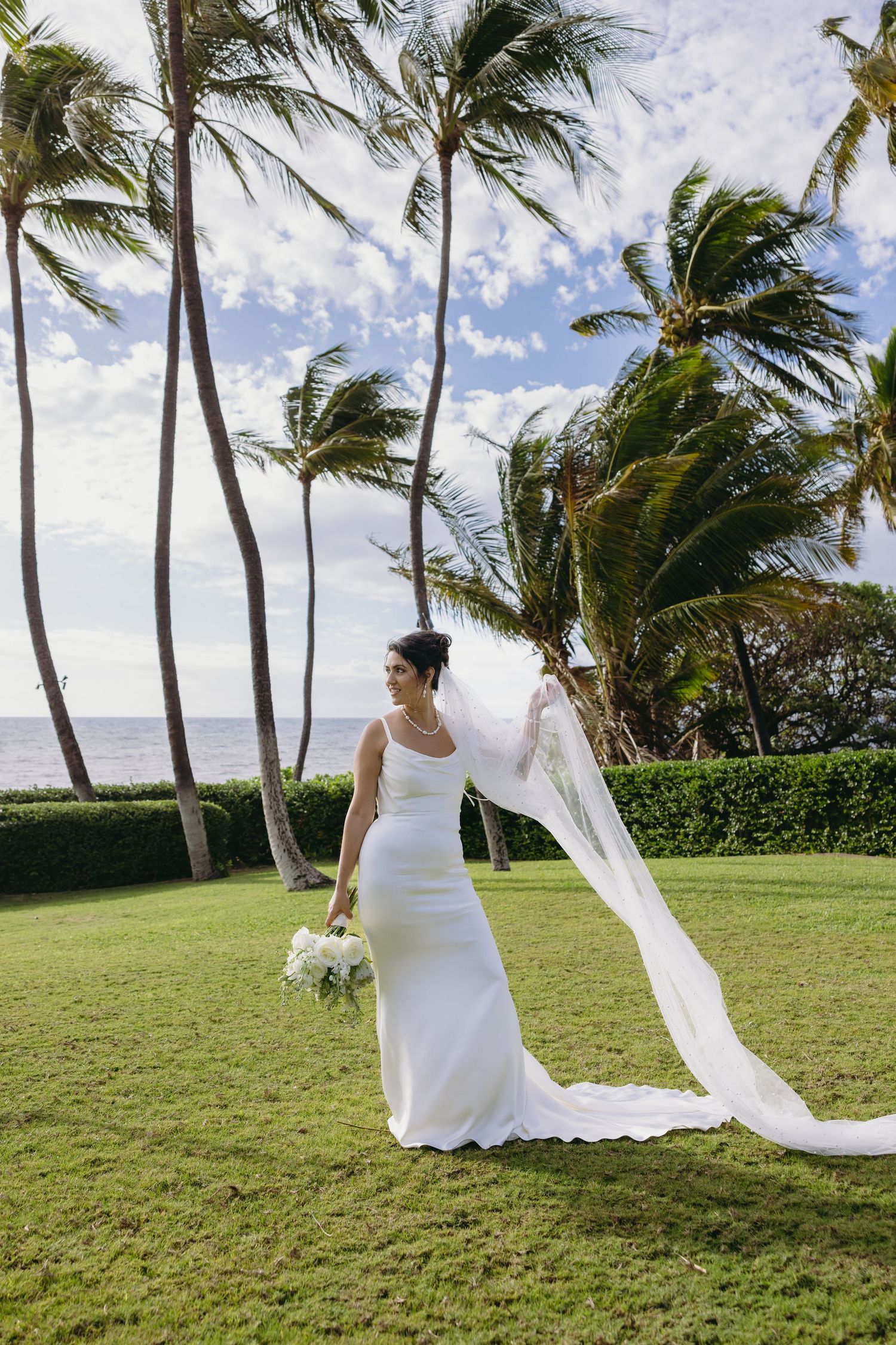 Wedding dress veil flowing in the wind against palm trees on a tropical beach.
