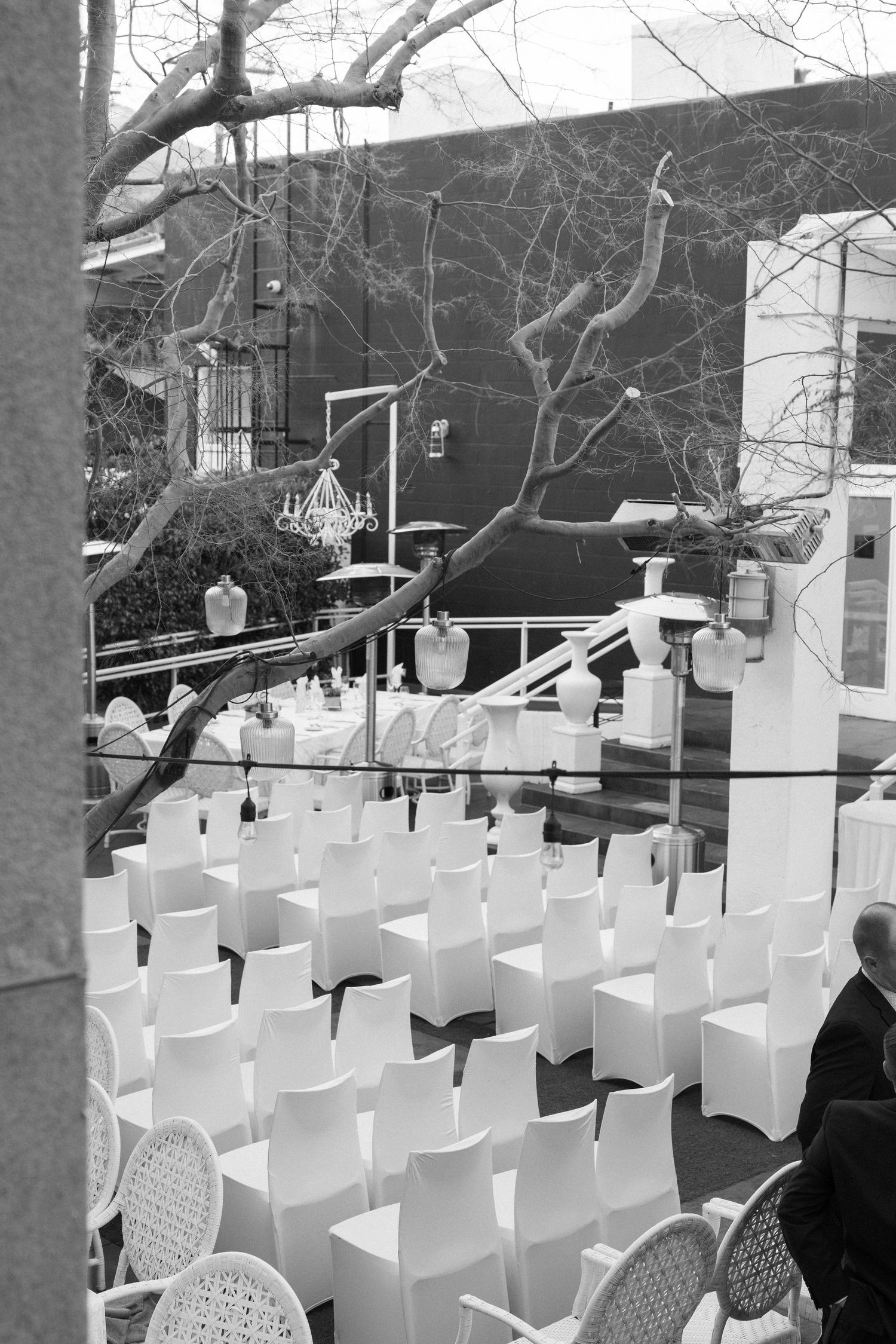 Black and white photo of outdoor wedding ceremony setup with rows of white chairs in a courtyard.