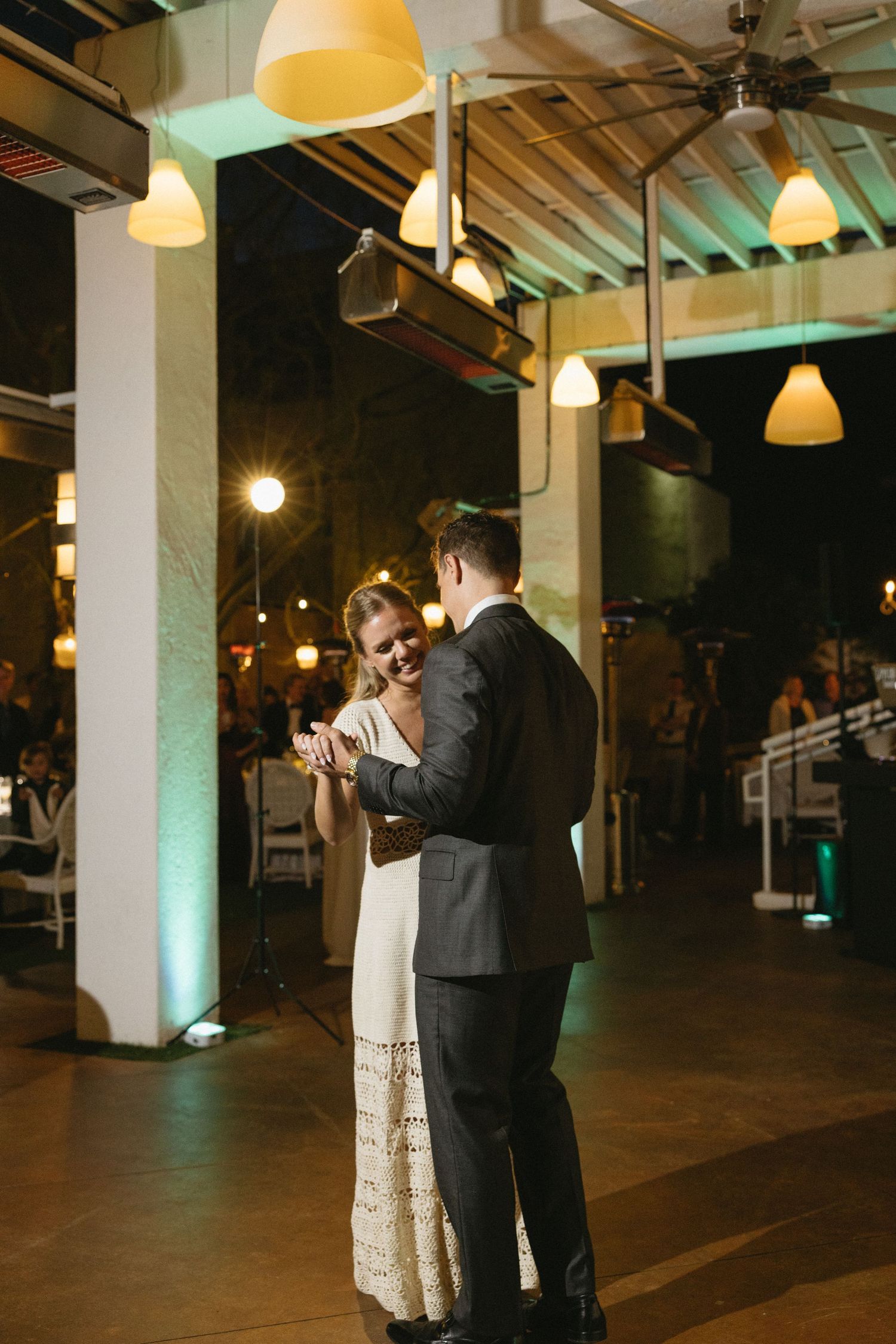 Bride and groom share their first dance at an elegant indoor wedding reception with warm pendant lighting.