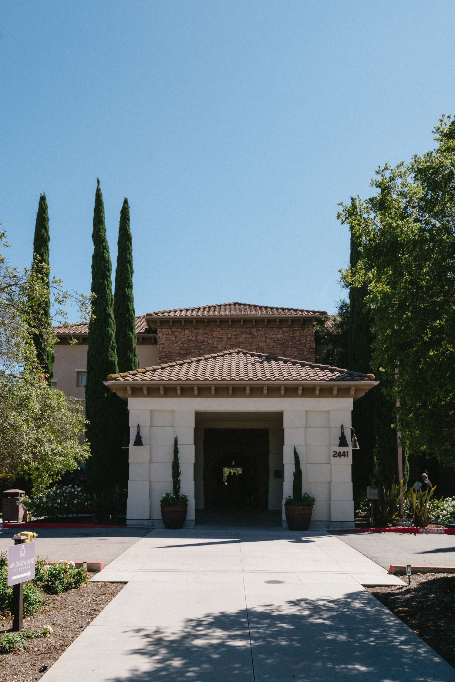 Elegant winery entrance with Italian cypress trees, terracotta roof, and manicured grounds under a clear blue sky.