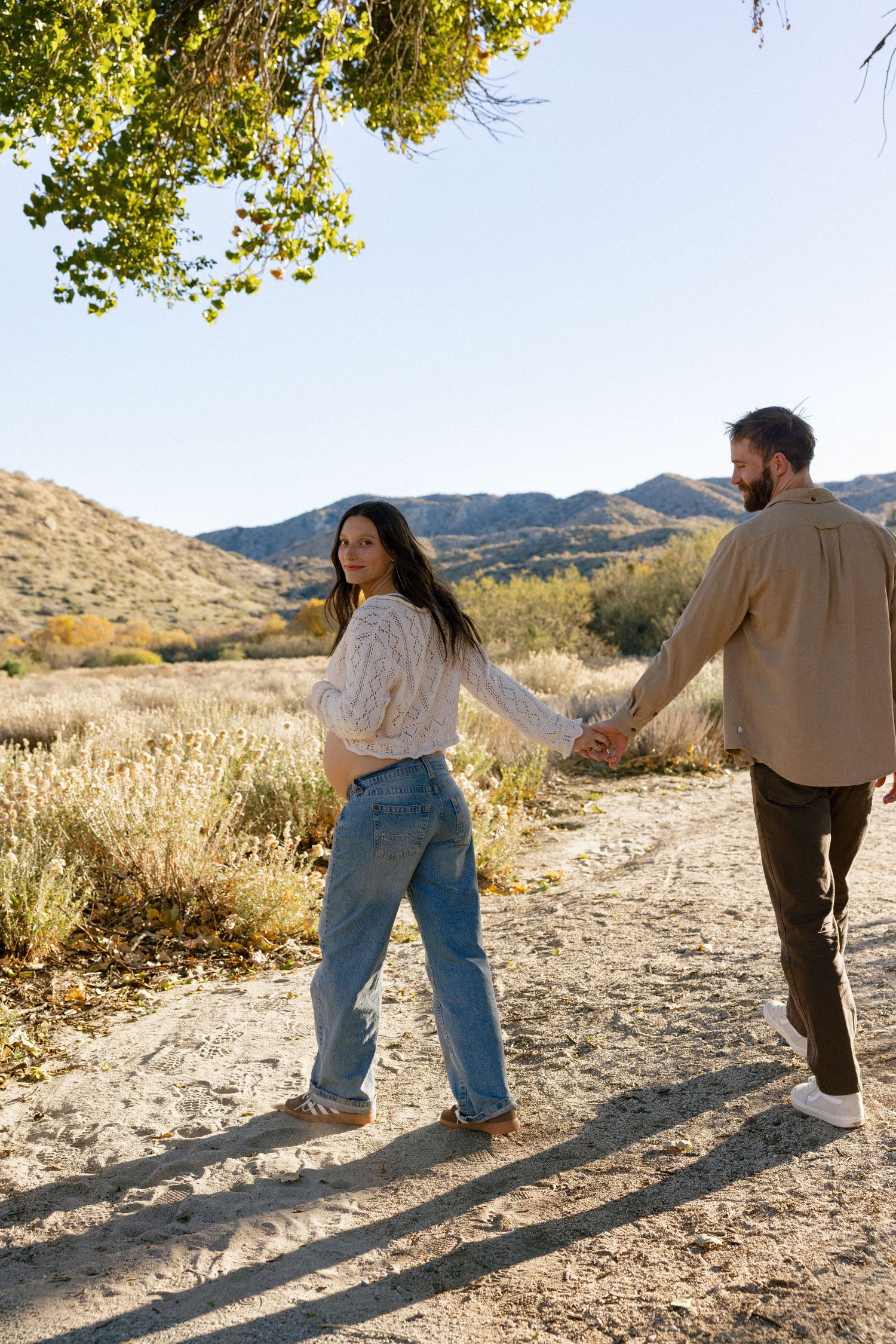 Playful couple walking away on desert path with long shadows in afternoon light.