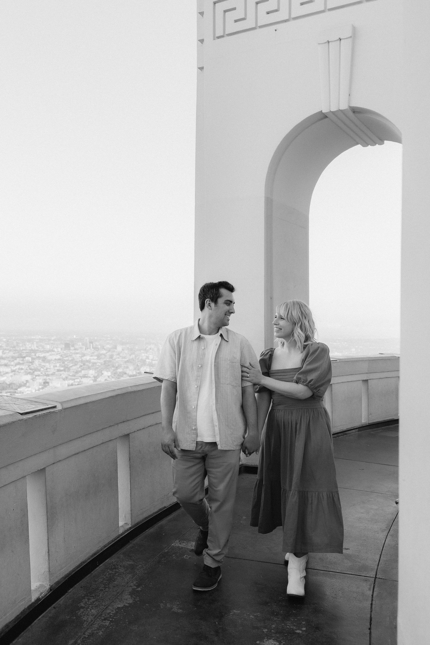 Couple sharing a moment in an elegant white archway overlooking a cityscape.