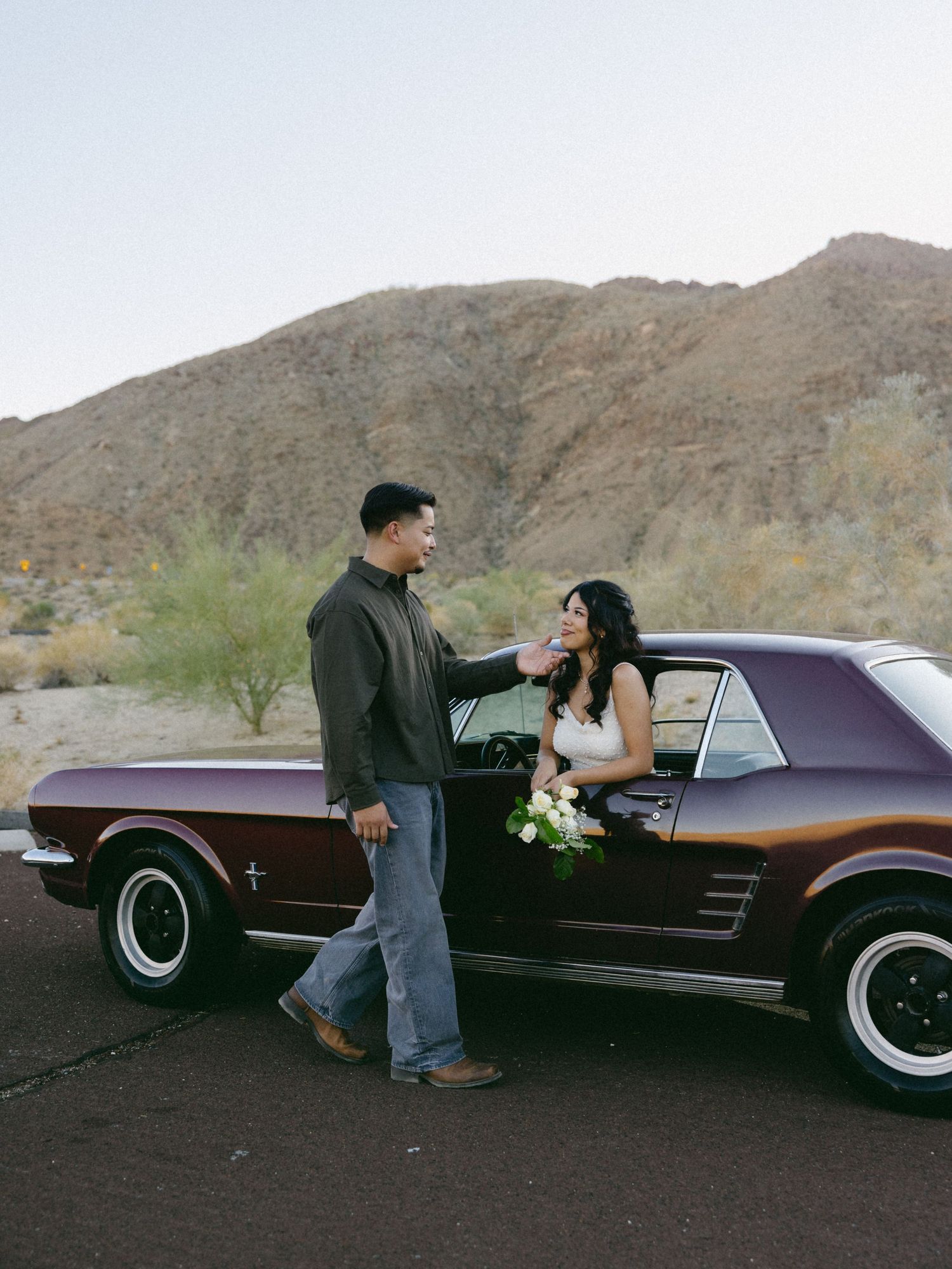Desert engagement session featuring couple with classic burgundy car.