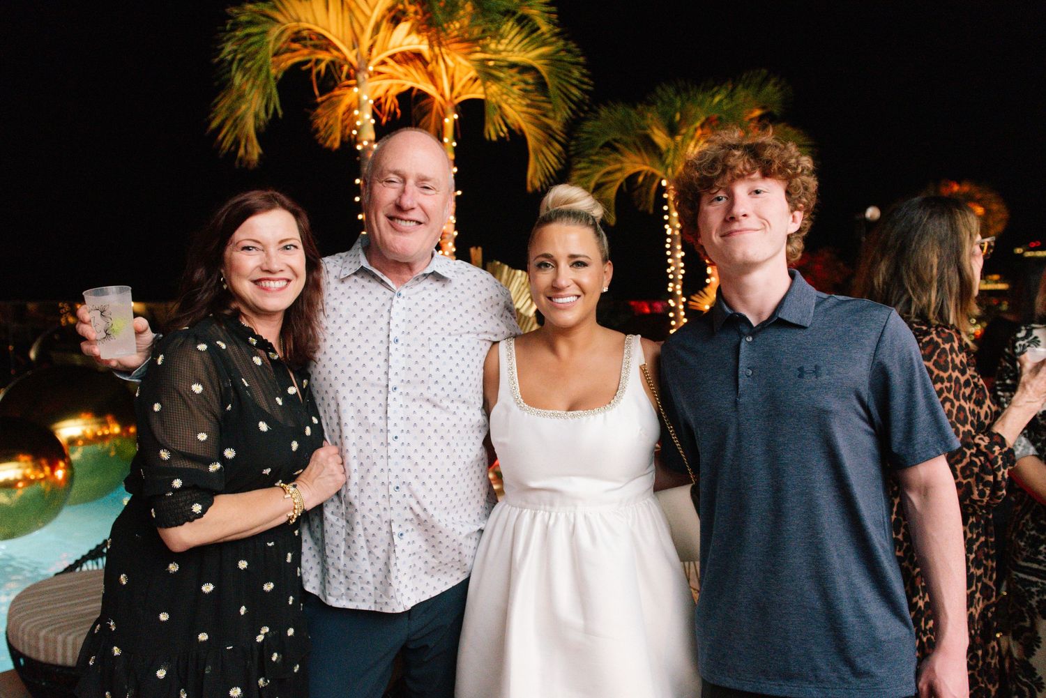 Group of guests posing together at a nighttime outdoor celebration with palm trees.