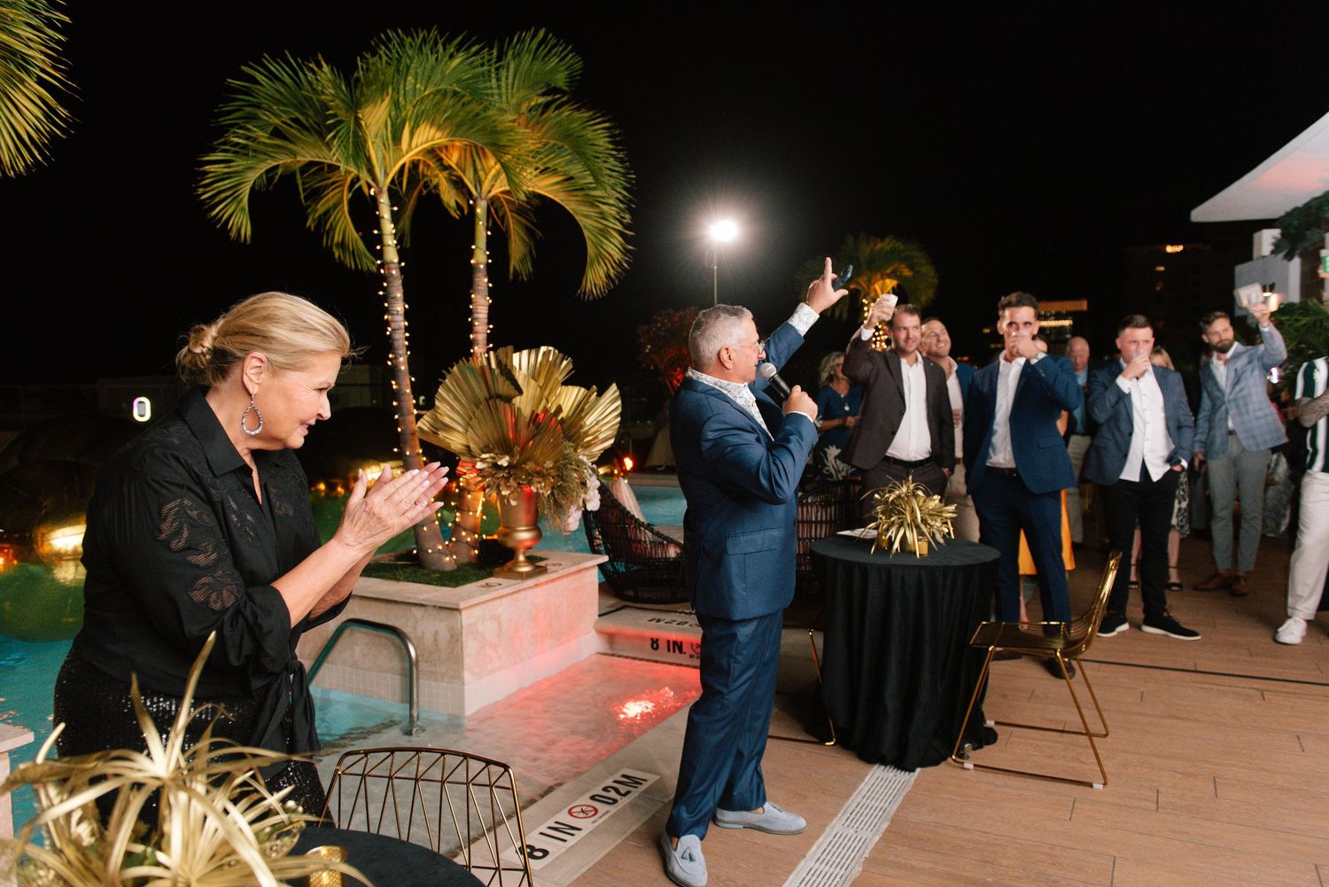 Evening poolside event with palm trees and decorative lighting.