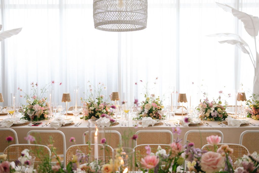 Airy wedding reception setup with white chairs and romantic floral centerpieces.