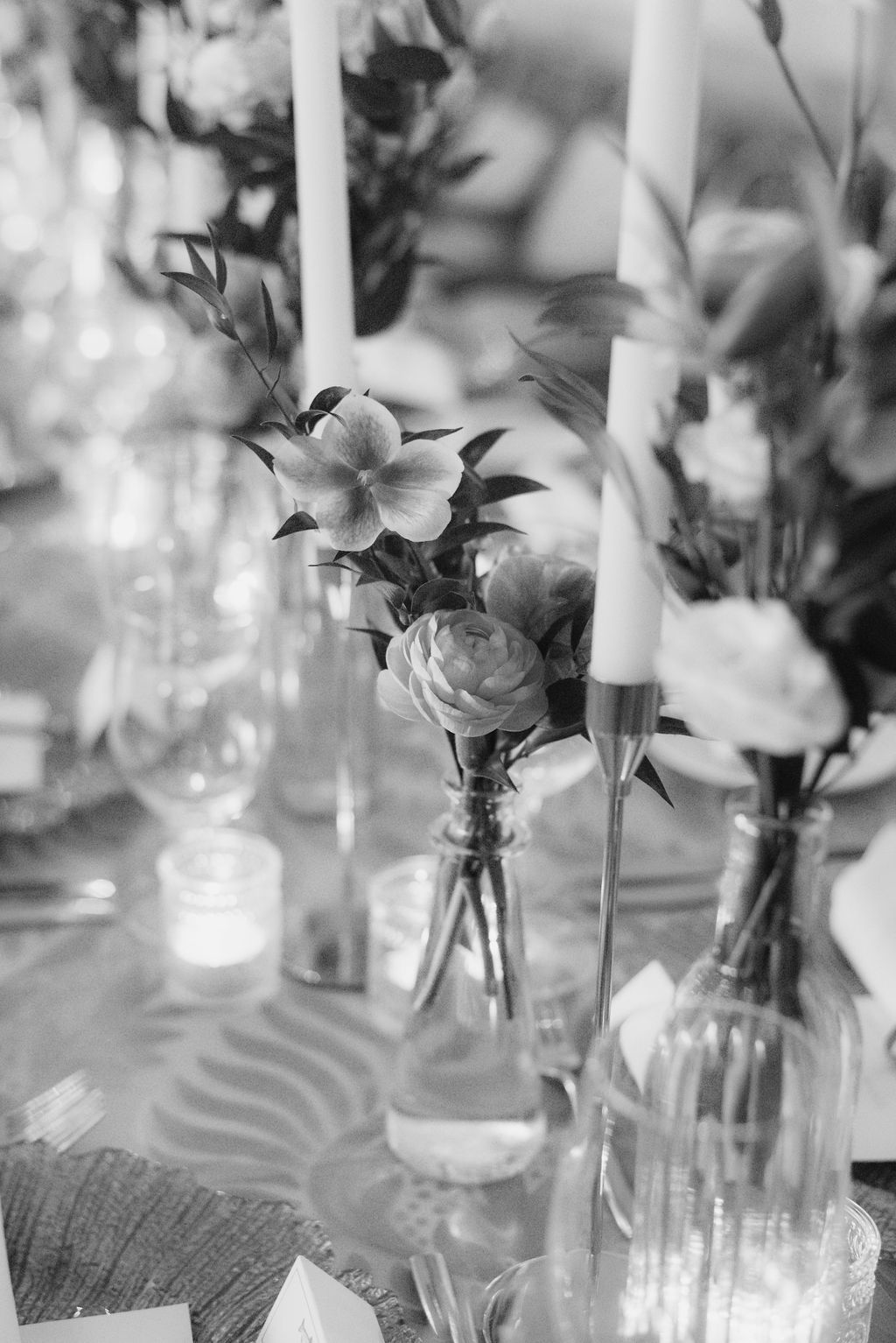 Black and white detail of floral centerpieces with white candles on an elegant dining table.