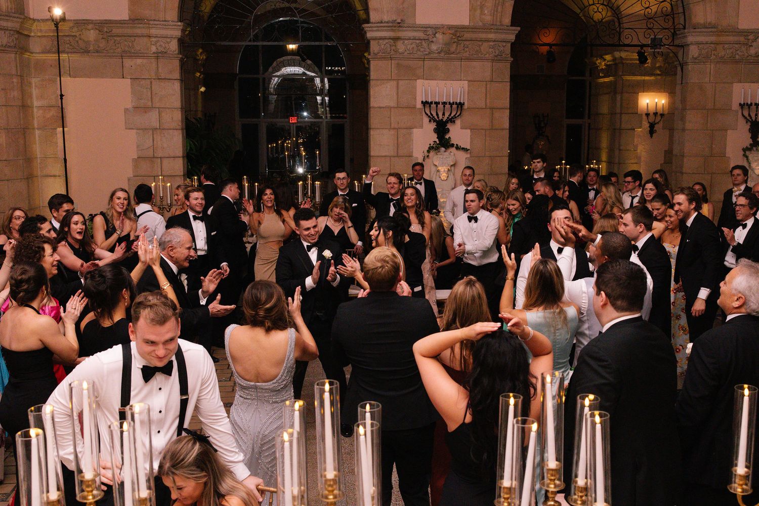 Large wedding celebration in a grand ballroom with stone columns and formal attire.