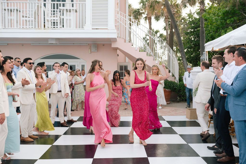 Wedding celebration on a checkered dance floor with guests in pink and white attire.