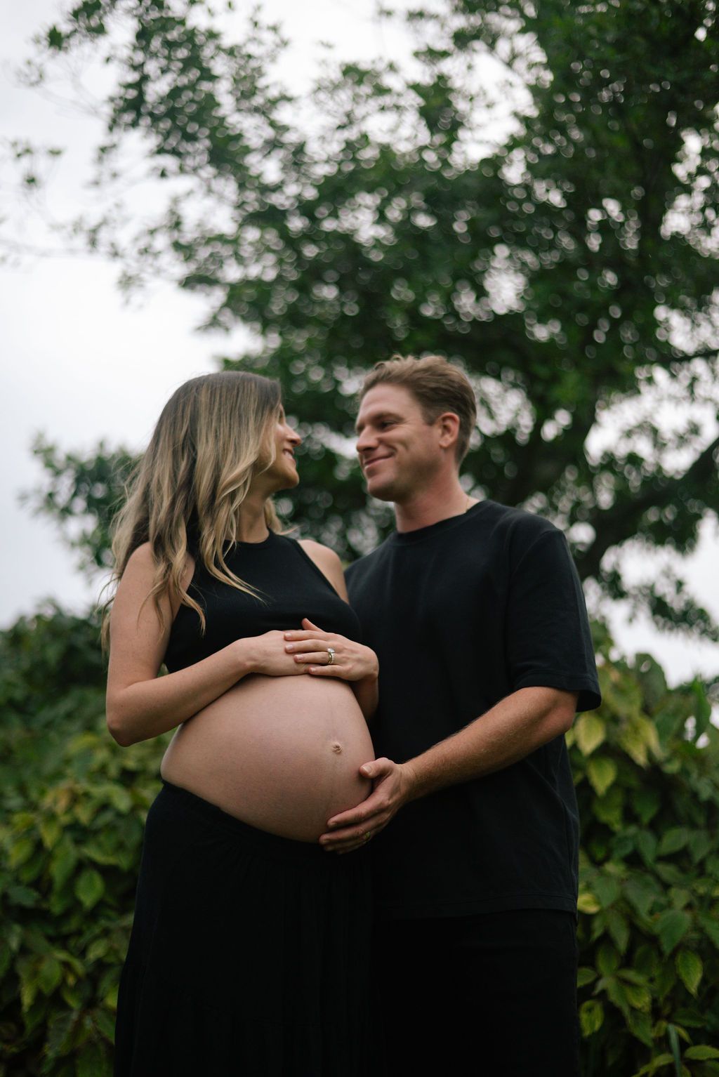 Maternity photo shoot captures intimate moments between couple in black attire outdoors.