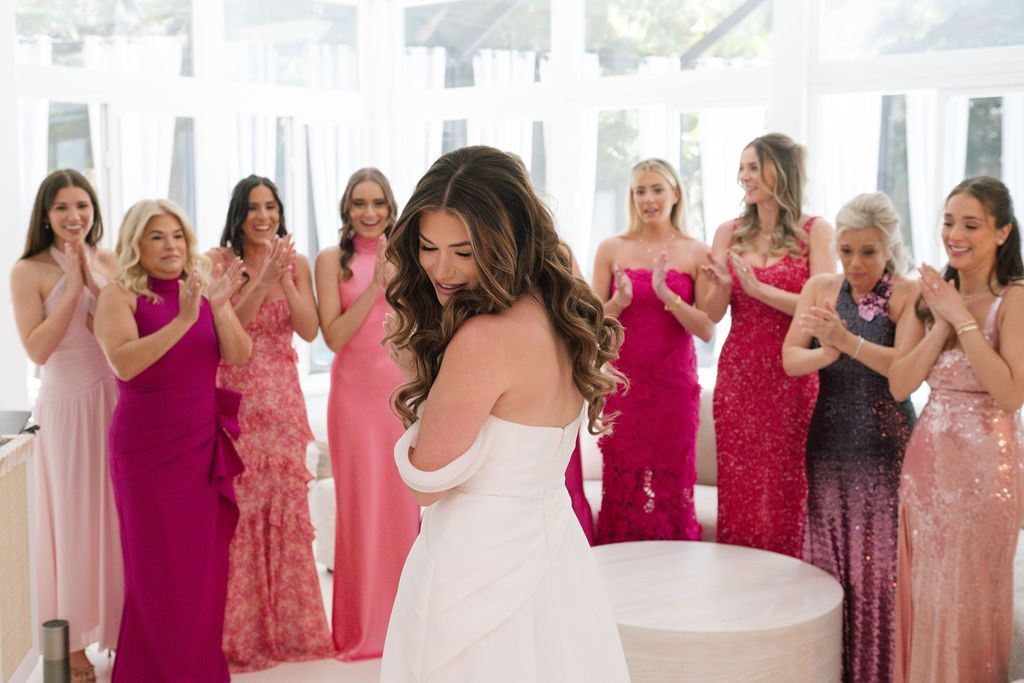Wedding party in pink and burgundy dresses reacting with joy during celebration.