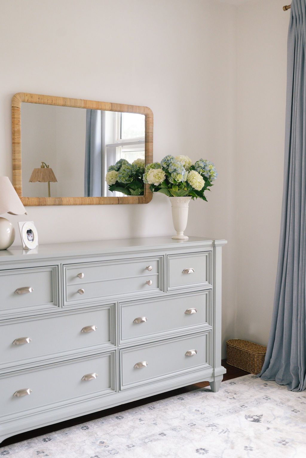 White dresser with brass handles decorated with mirror and floral accents in neutral nursery.