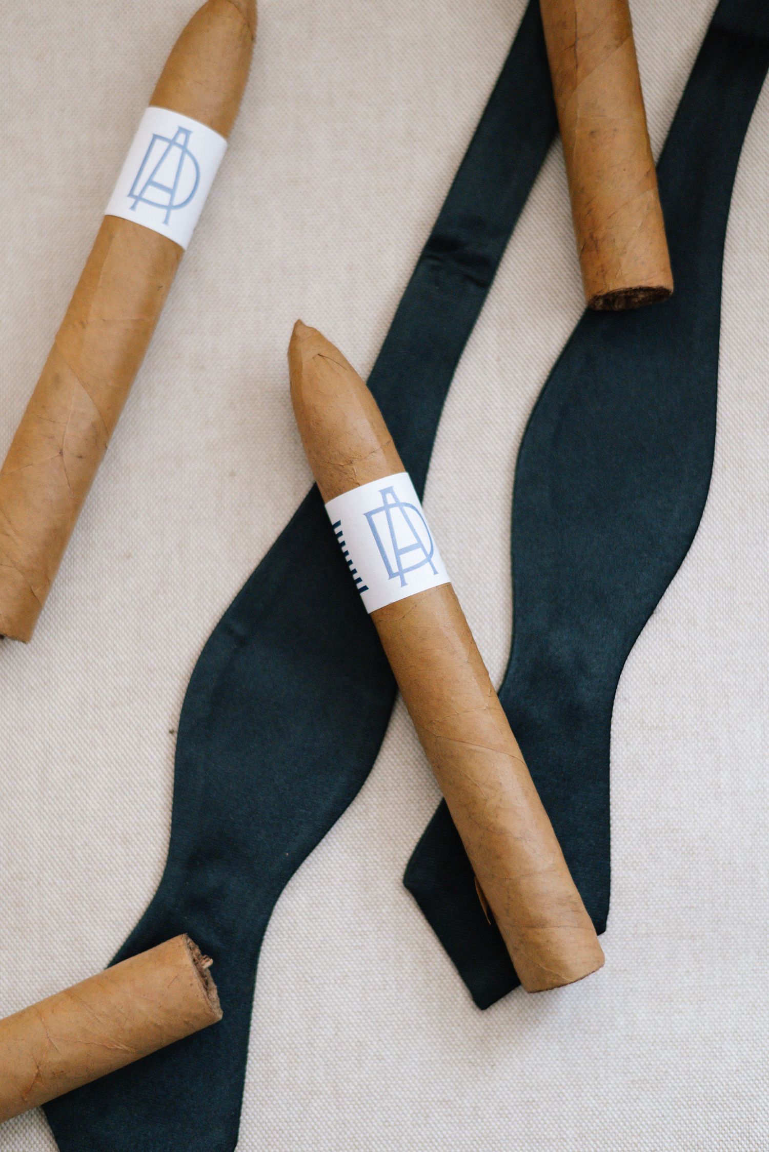 Multiple brown cigars arranged diagonally with black ties on beige background.