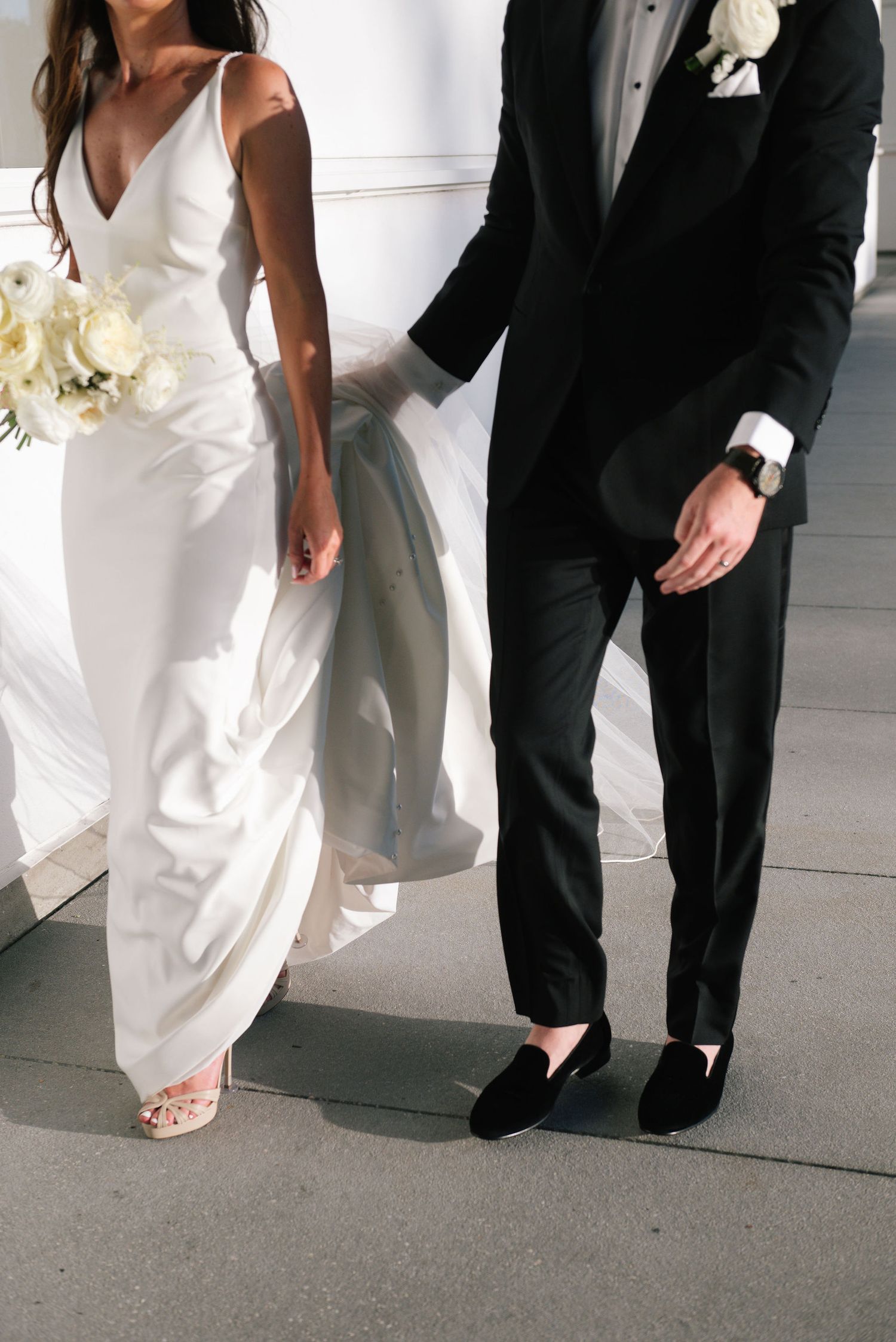 Close-up details of a bride and groom's formal attire showing white dress and black tuxedo.