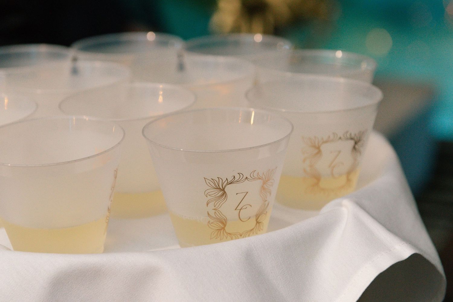 A row of white plastic cups filled with a pale yellow liquid sit on a dark surface.