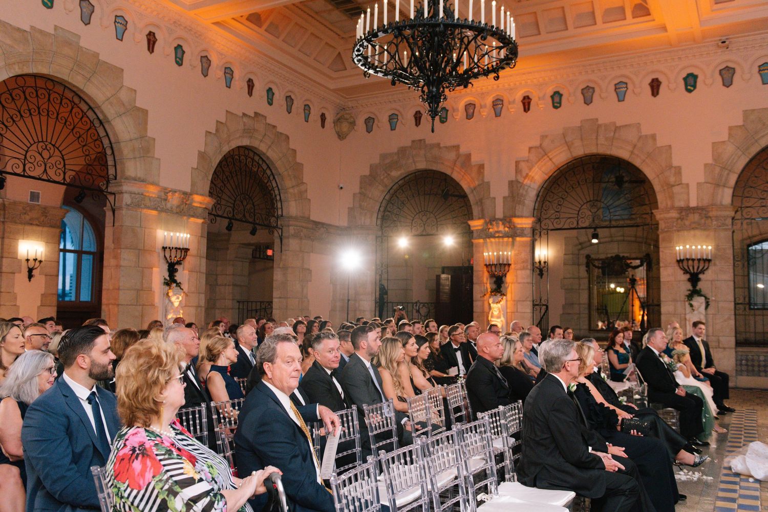 Guests seated in ornate golden ballroom during elegant wedding ceremony.
