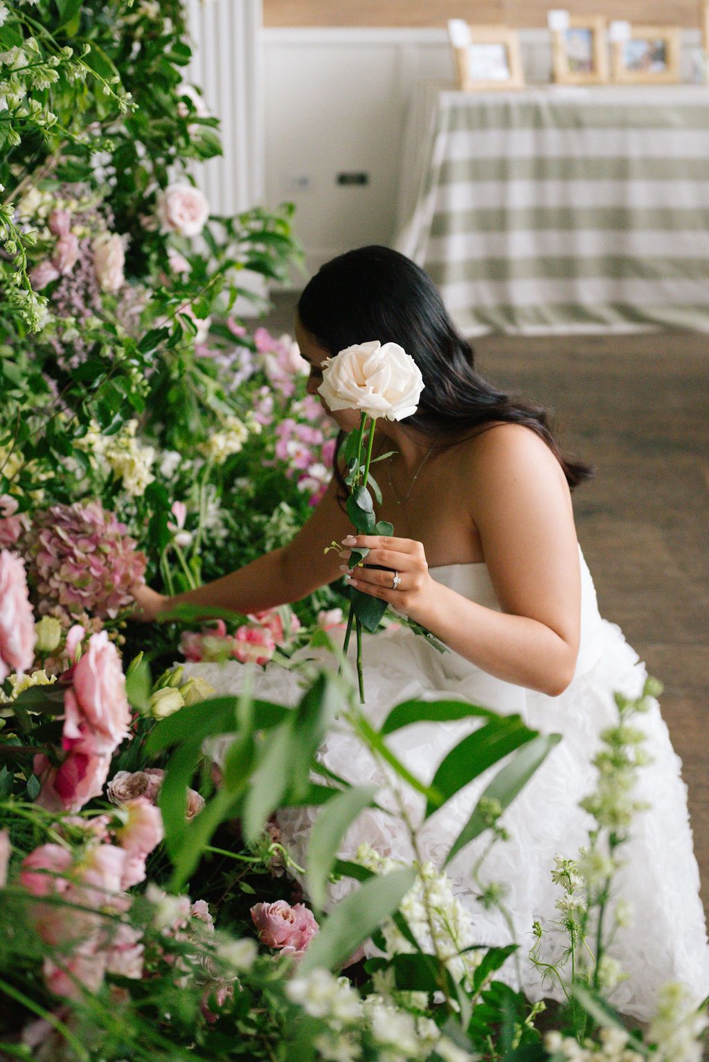 Person in white dress posing among pink and white floral arrangements.