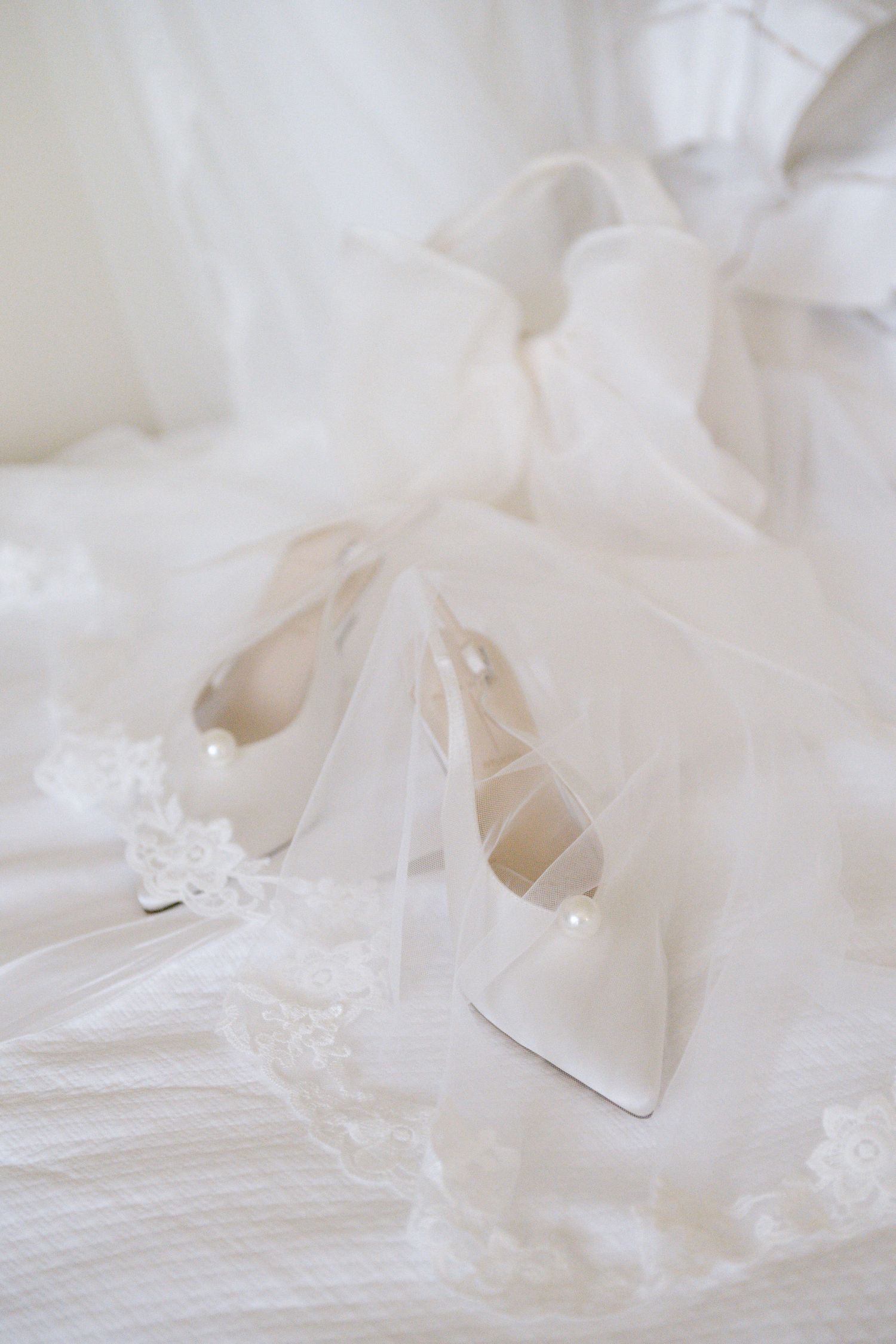 White bridal heels with delicate lace veil on light fabric background.