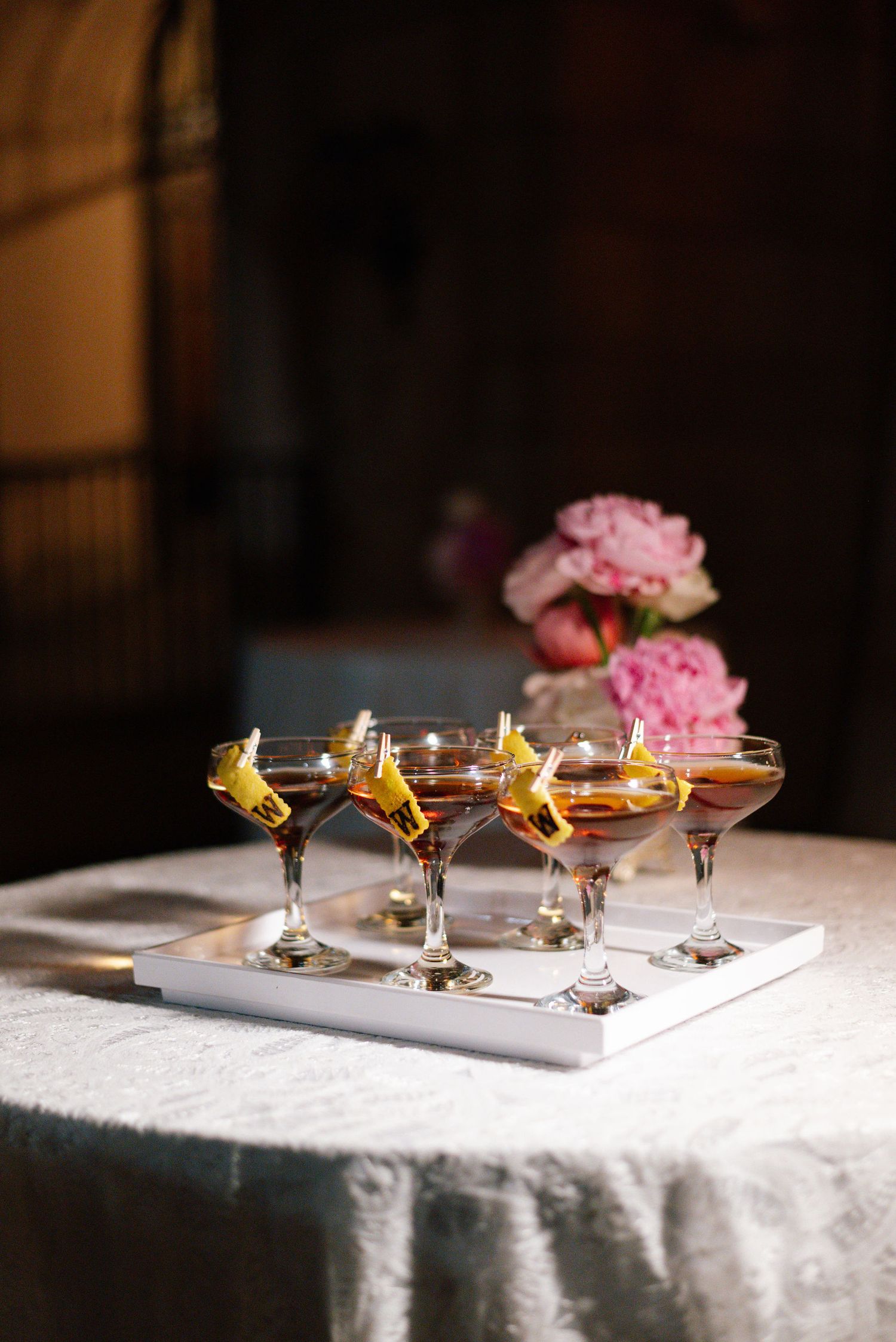 Elegant cocktails garnished with flowers and citrus arranged on a white tablecloth at an upscale event.