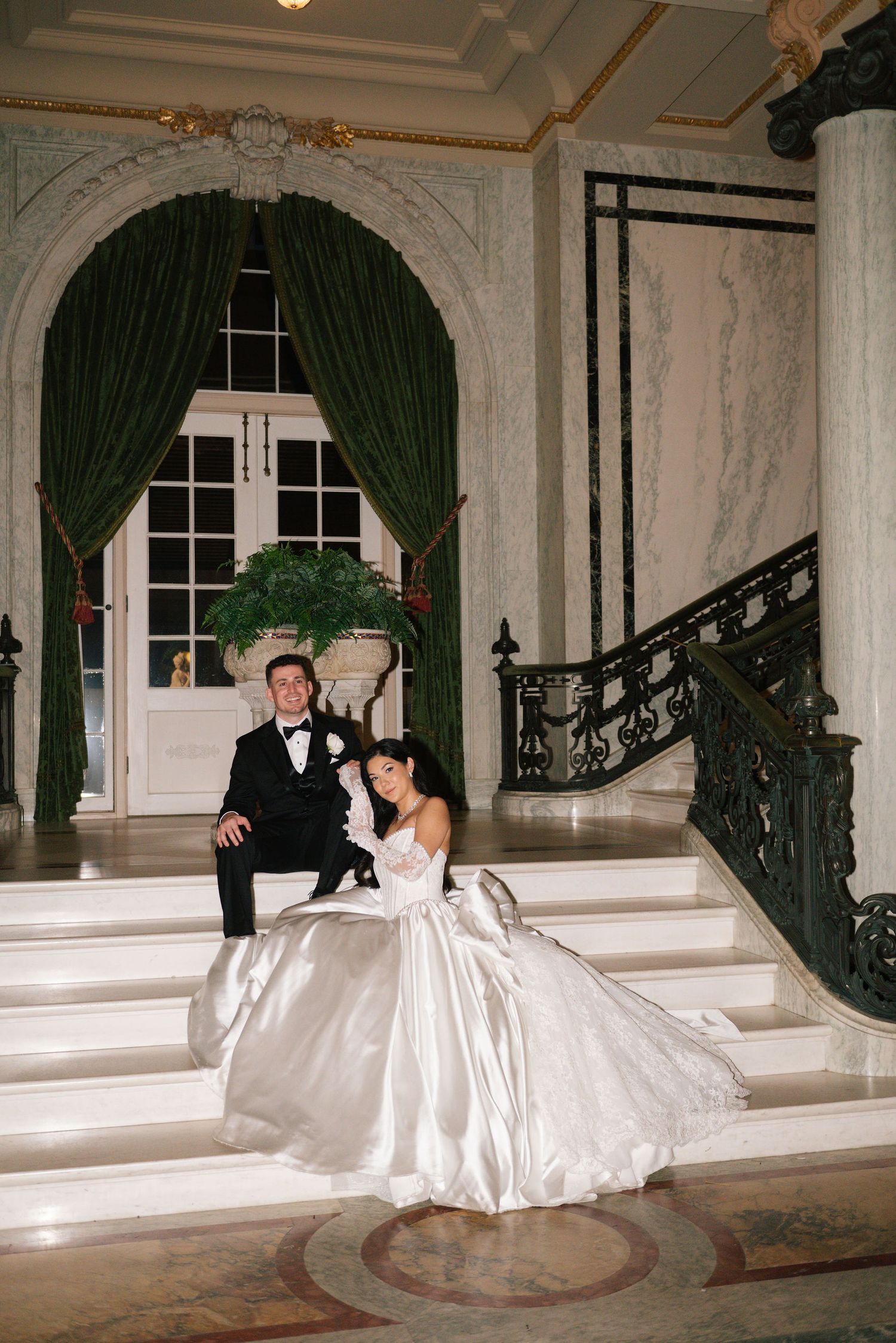 A couple poses playfully on elegant marble steps with decorative railings.