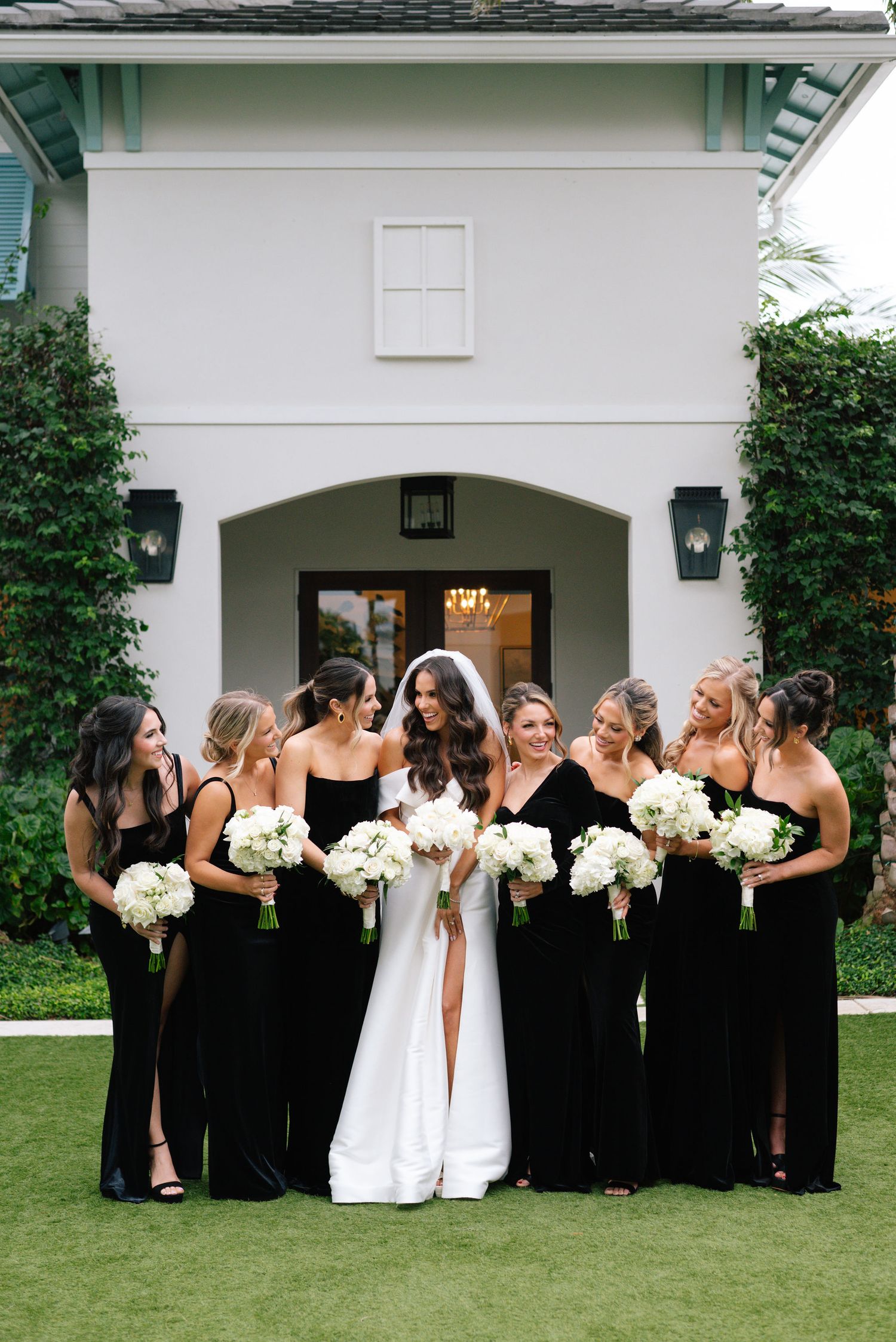 Bridal party gathered for candid photos outside white building with palm trees.