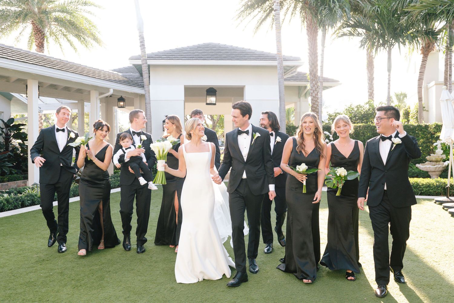 Wedding party in black and white attire posing outdoors with palm trees.