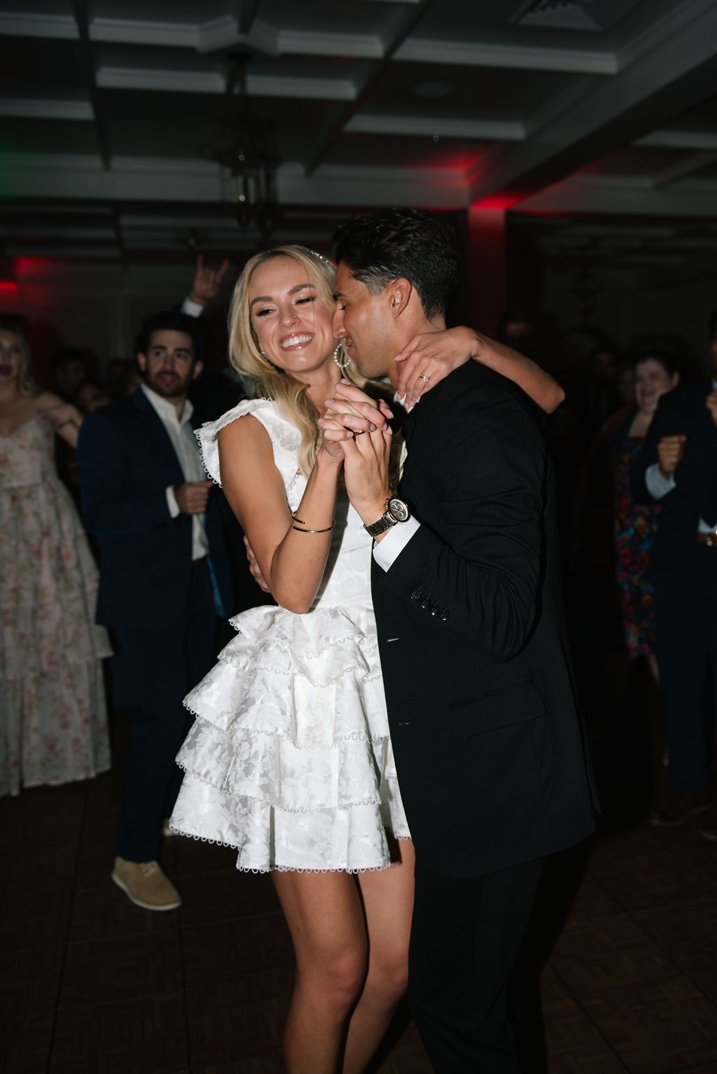 A couple shares a romantic dance moment at a wedding reception with the bride wearing a short white dress.