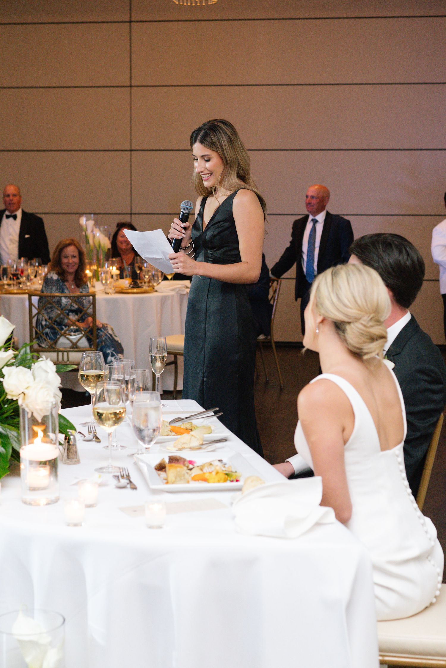 Wedding guests enjoy dinner at elegantly set tables with white linens.