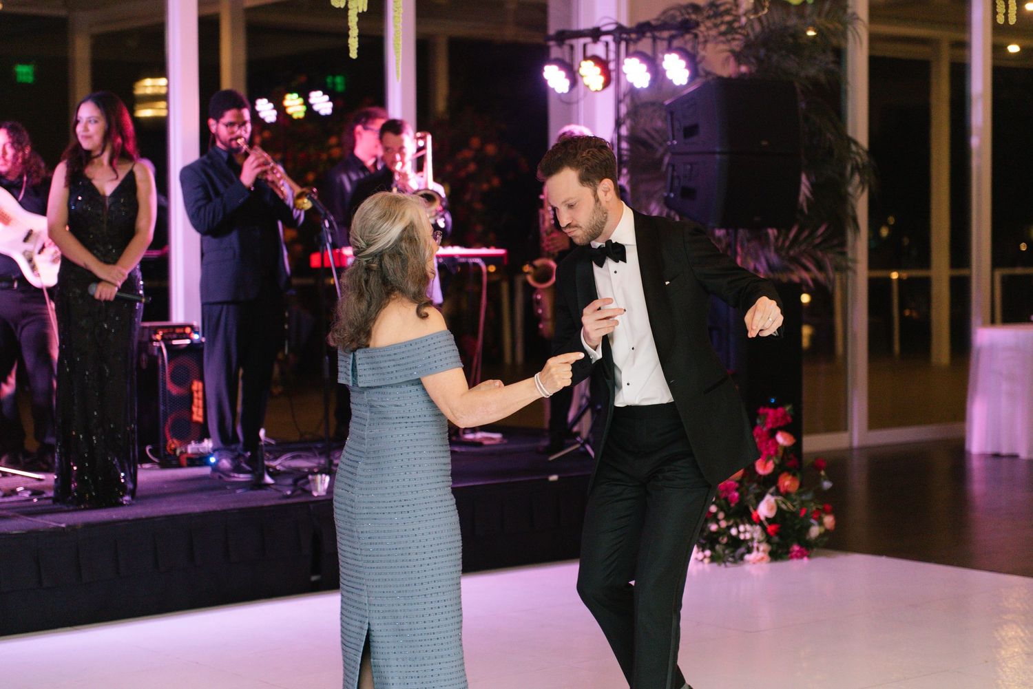 Couples slow dancing at an evening wedding reception with purple accent lighting and dark decor.